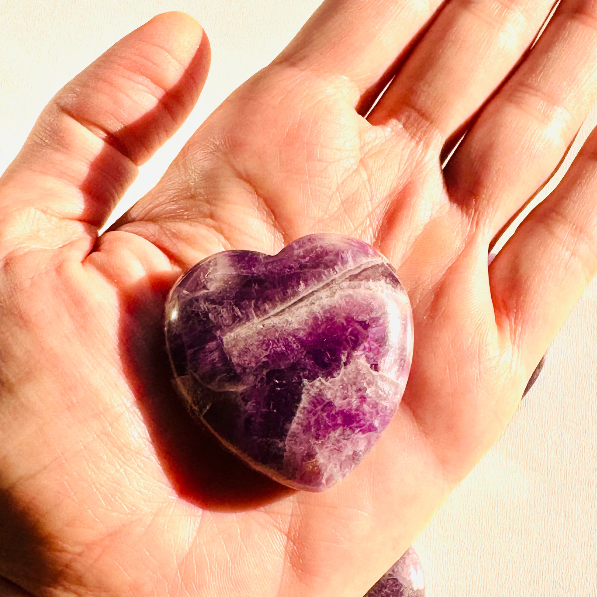 Heart-shaped purple crystal held in a hand against a light background