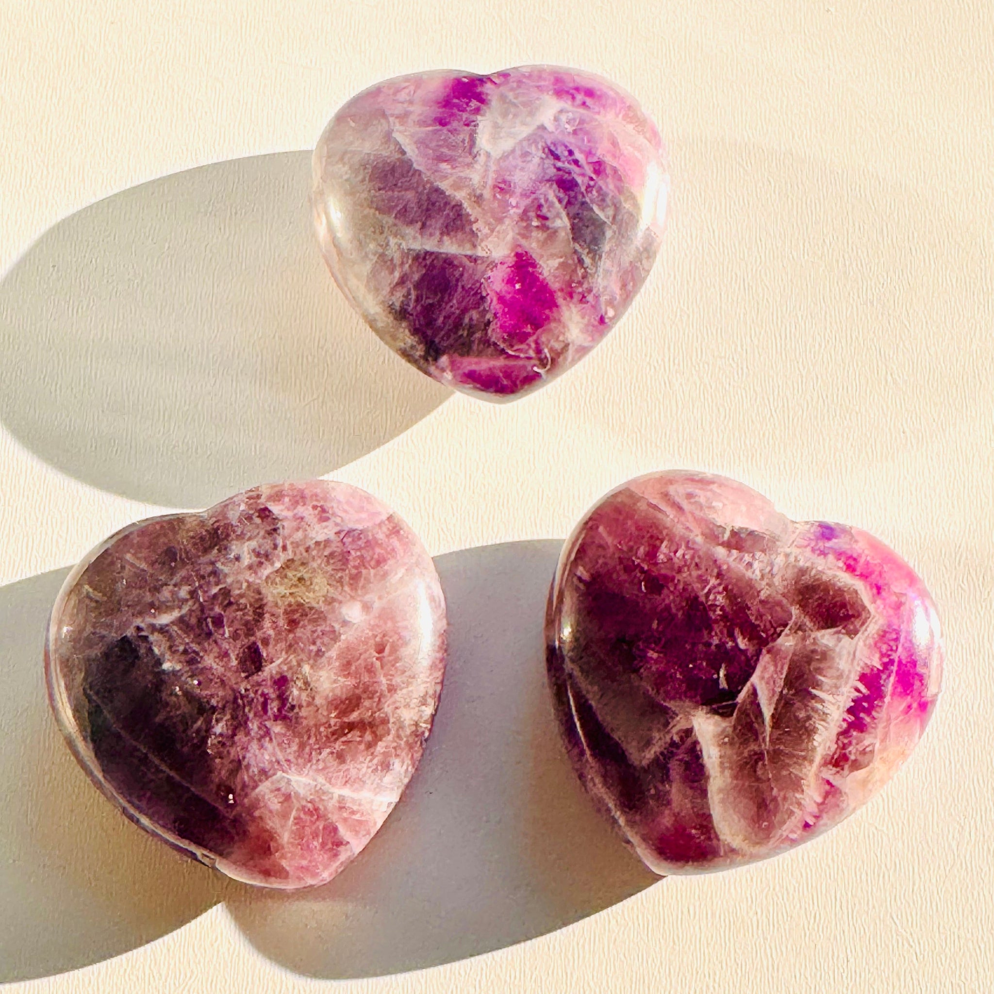 Three heart-shaped pink and purple stones on a beige background