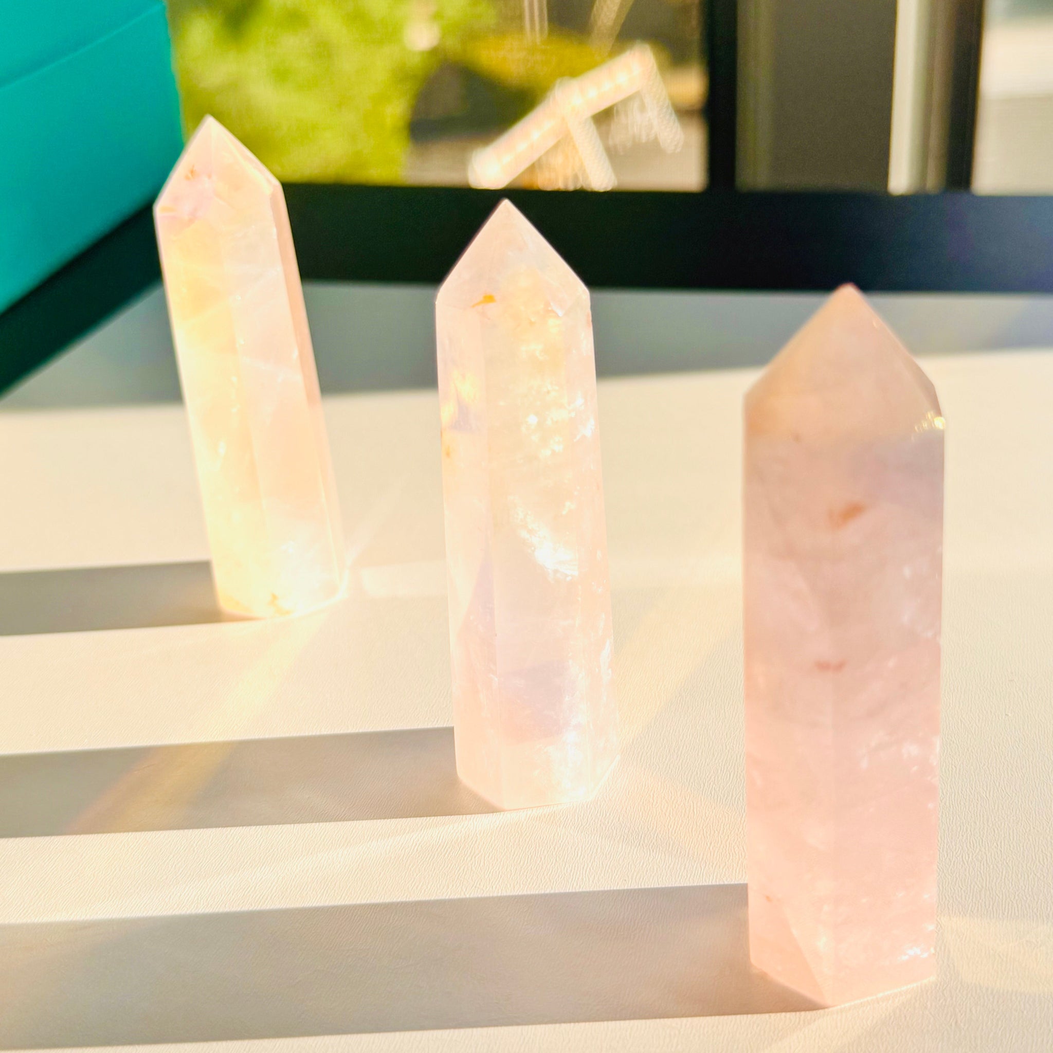 Three rose quartz crystal points on a reflective surface with a blurred outdoor background