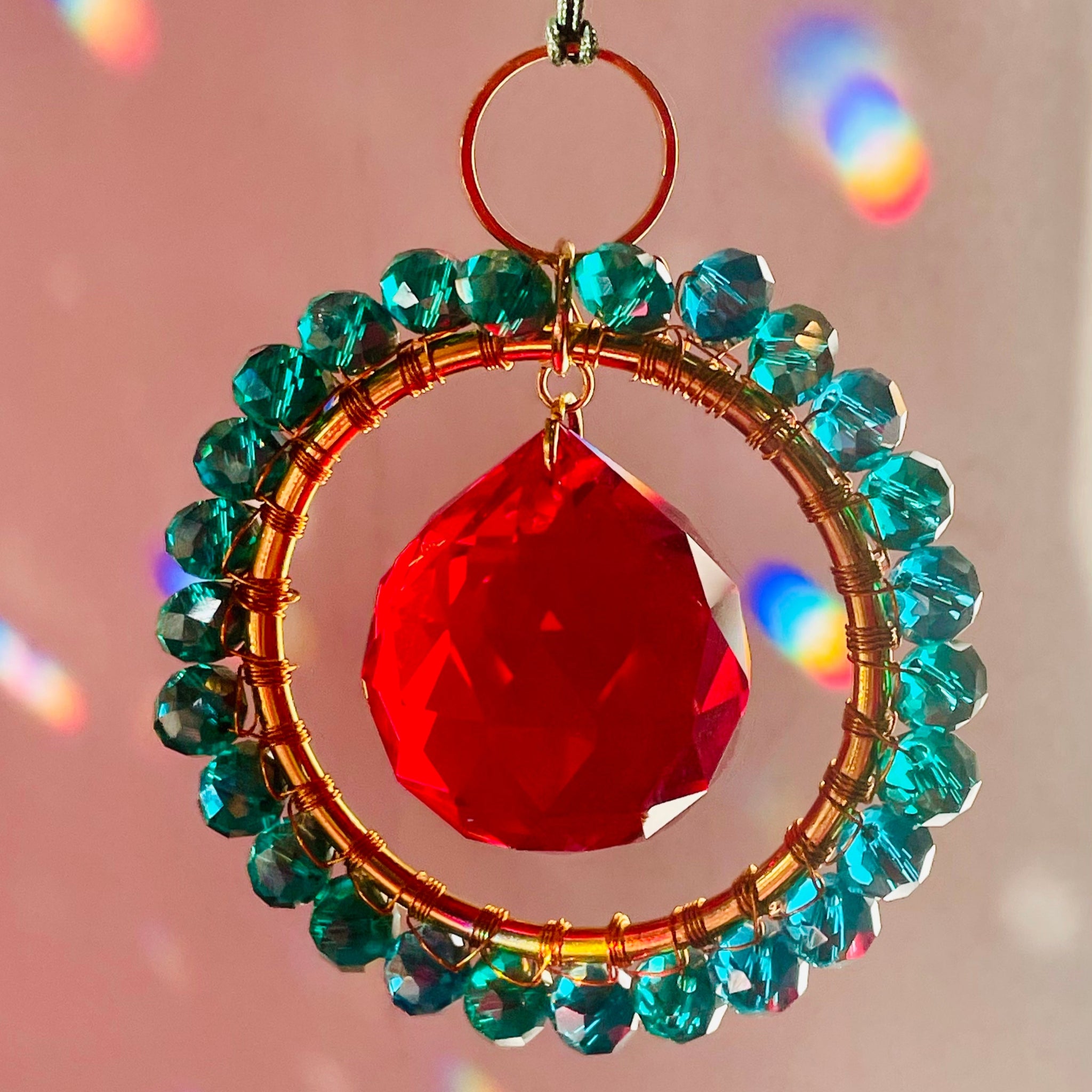 Decorative hanging ornament with red teardrop and green beads on a pink background