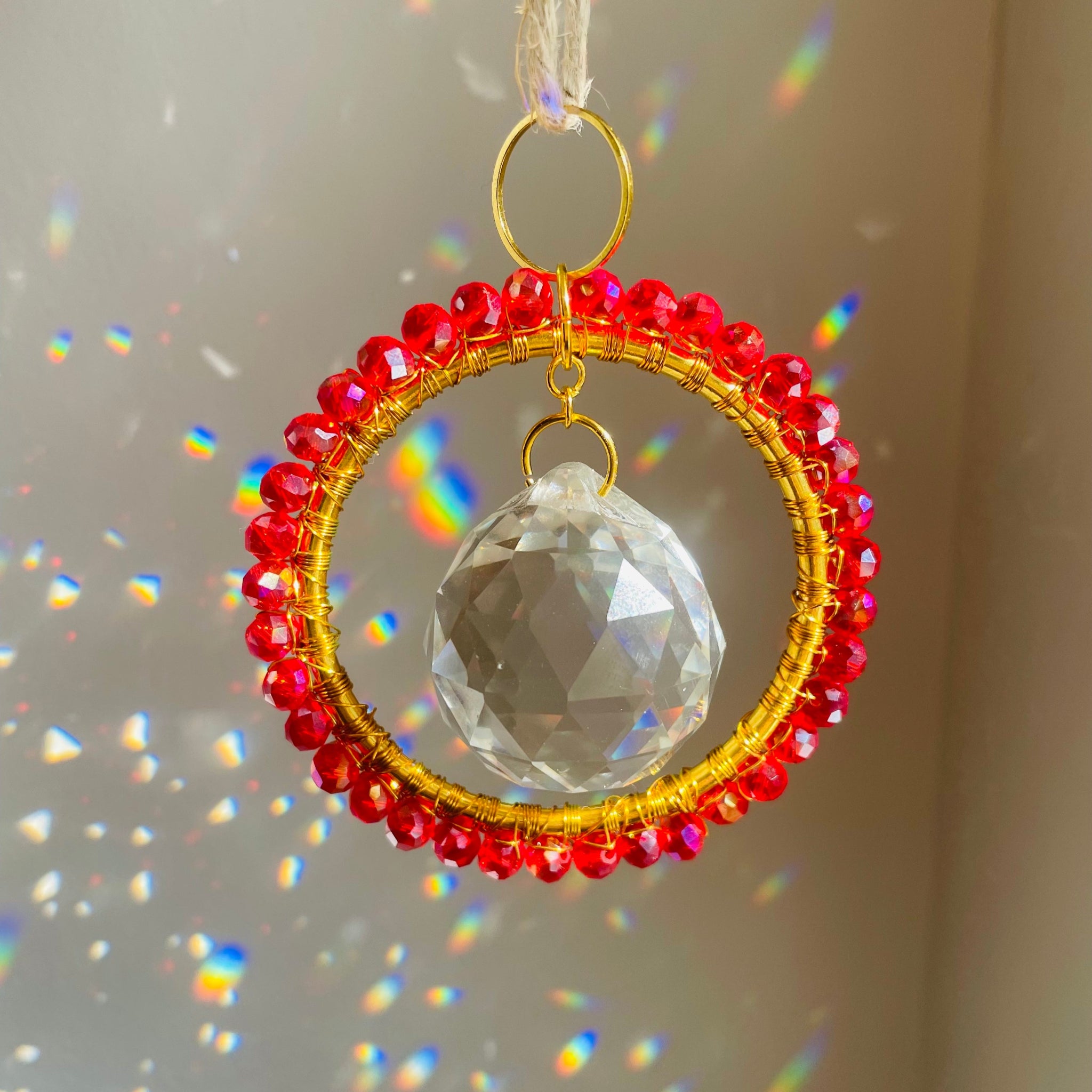 Decorative hanging ornament with red beads and a clear crystal ball on a neutral background