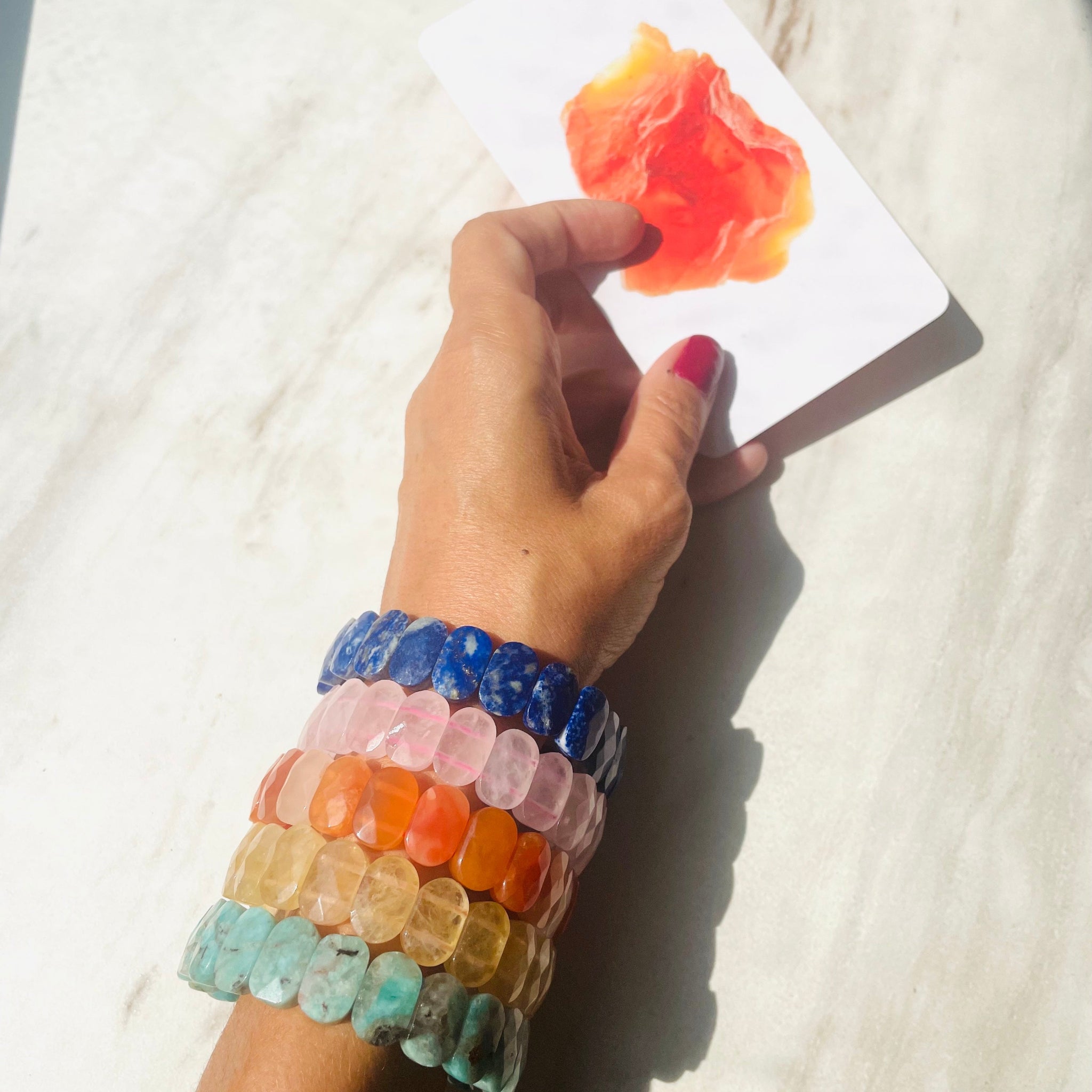 Chunky colorful gemstone bracelets on arm while hand is holding a card