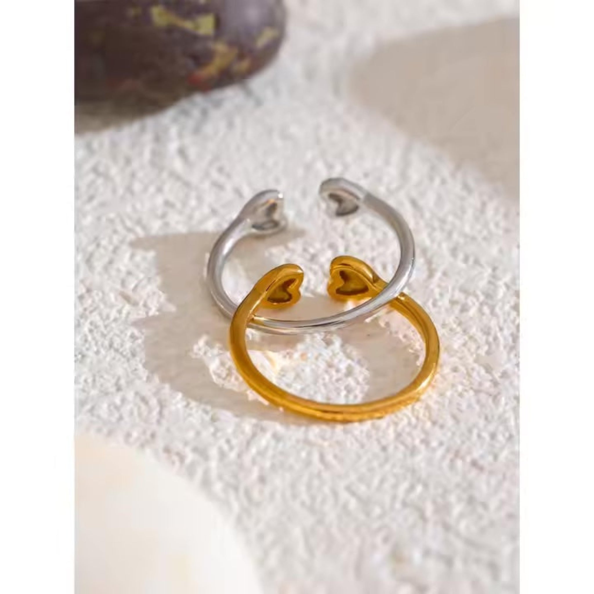 Two rings, one silver and one gold, on a textured white surface.