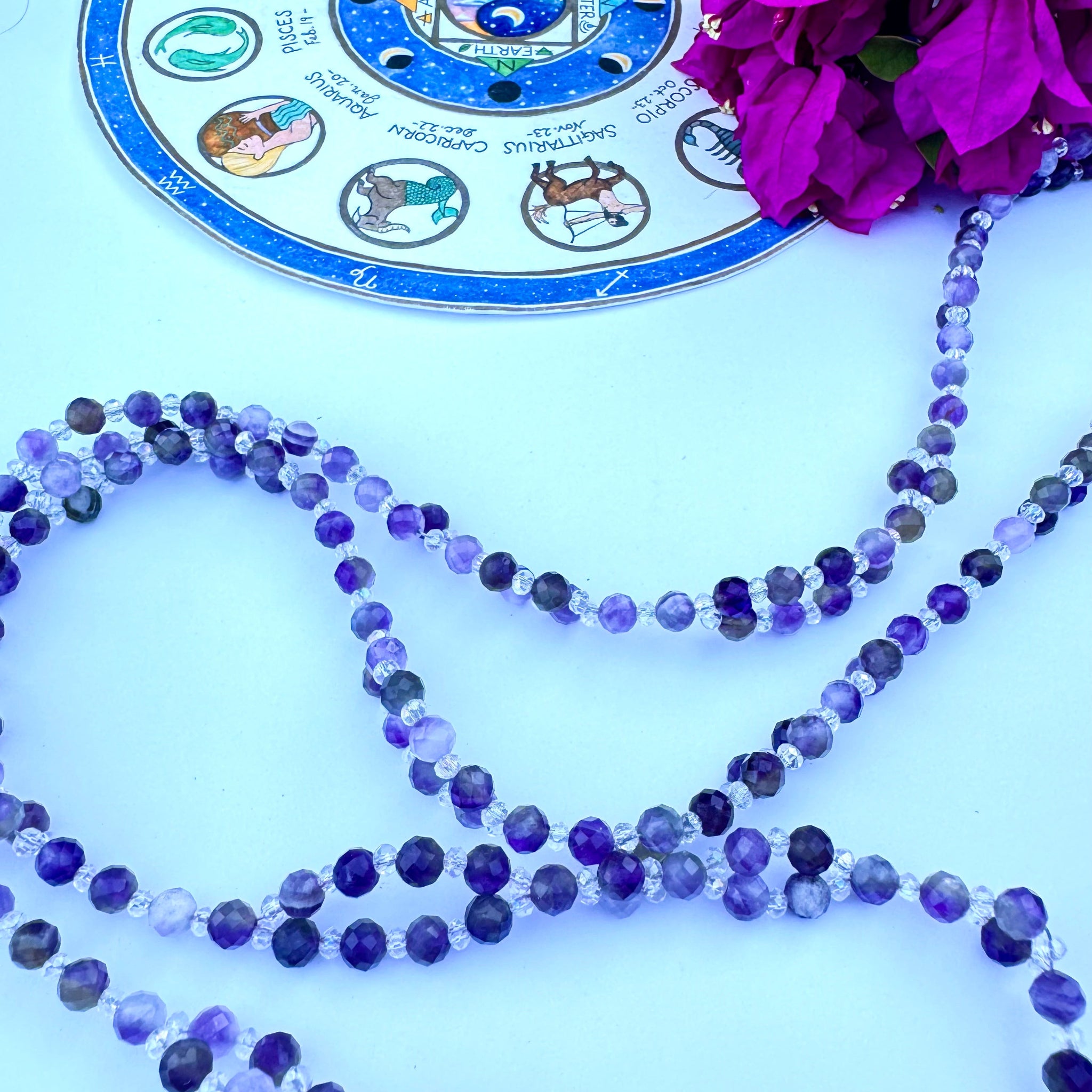 A tantric necklace with amethyst beads and a circular pendant featuring a sacred geometric pattern and a purple flower design.