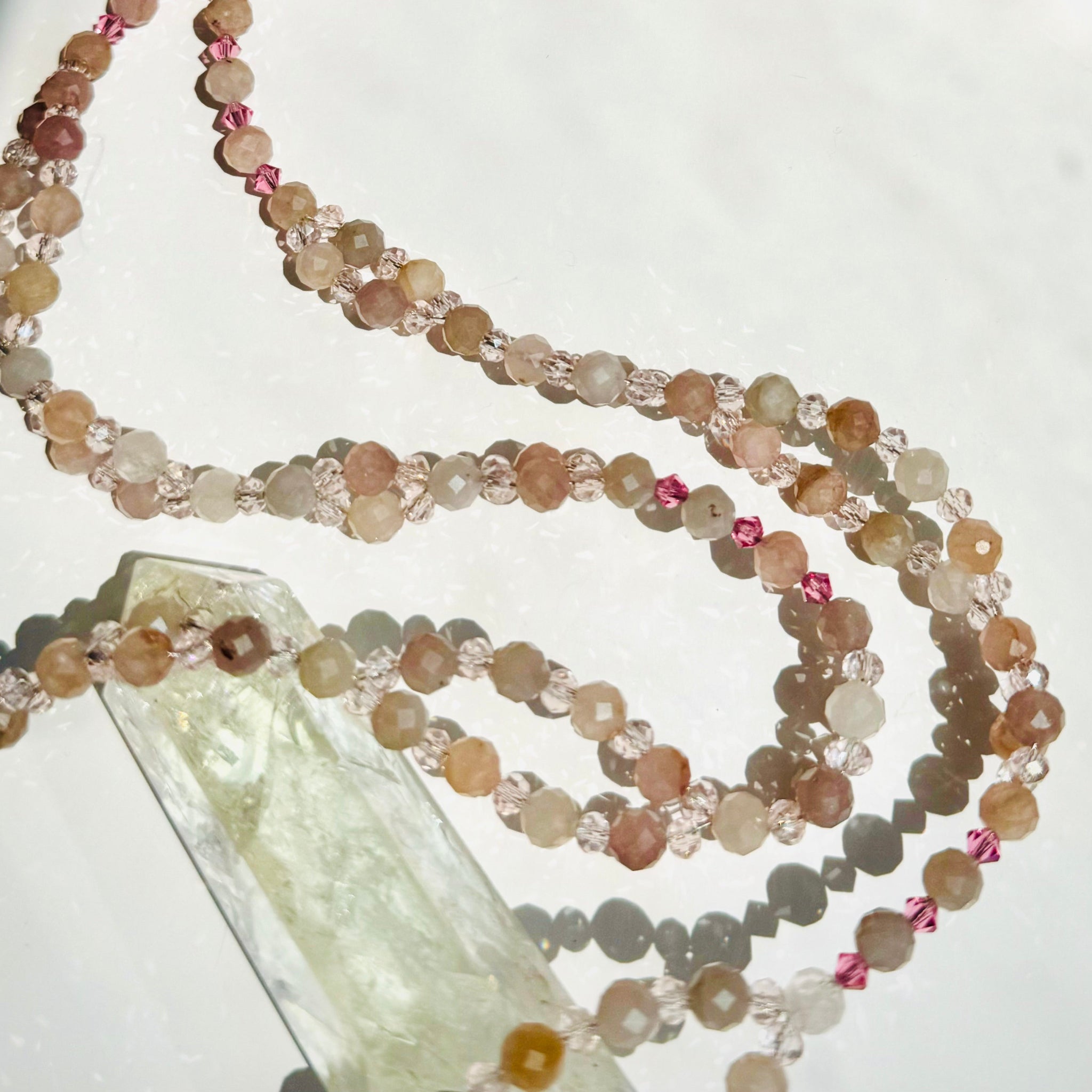 pink beaded necklace and crystal on white surface