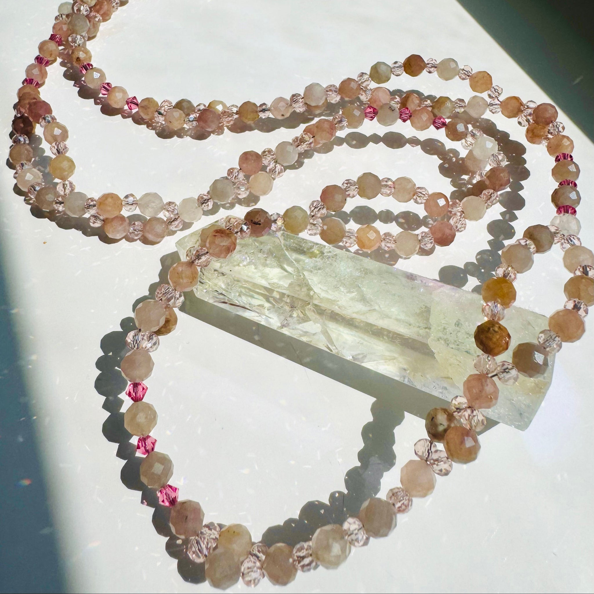pink beaded necklace on crystal photographed on white surface