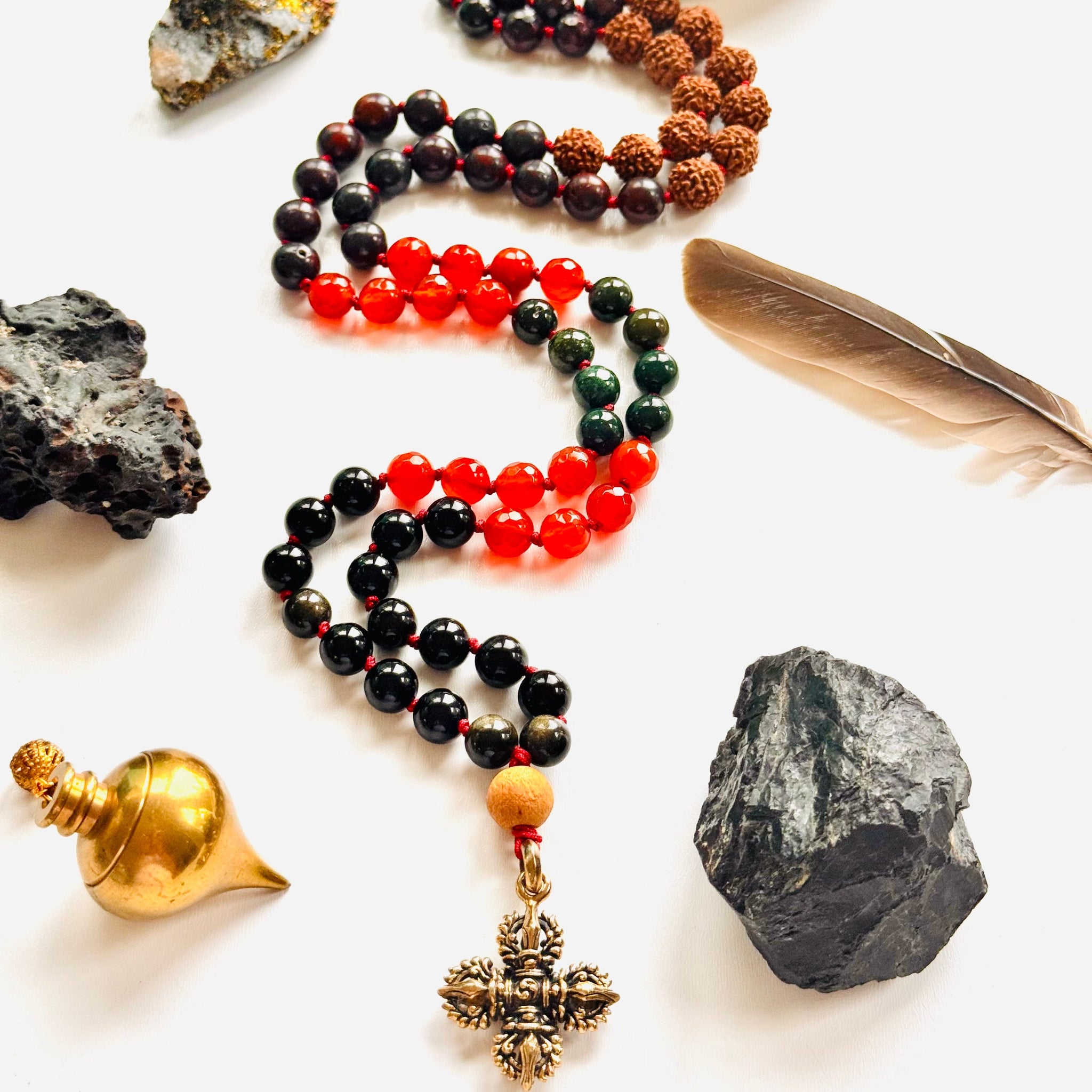 Necklace with beads and charms surrounded by stones, a shell, and a feather on a white background