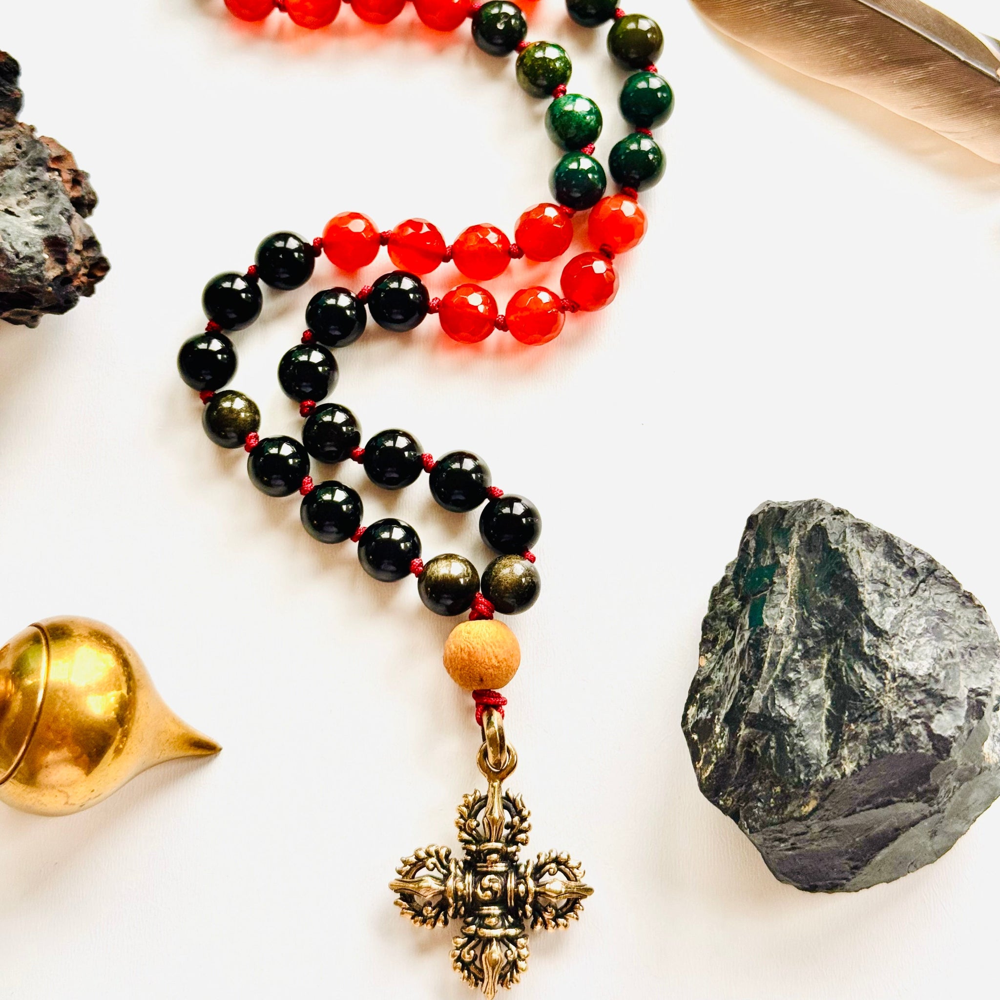 Multicolored beaded necklace with a cross pendant on a white surface with stones and a feather.