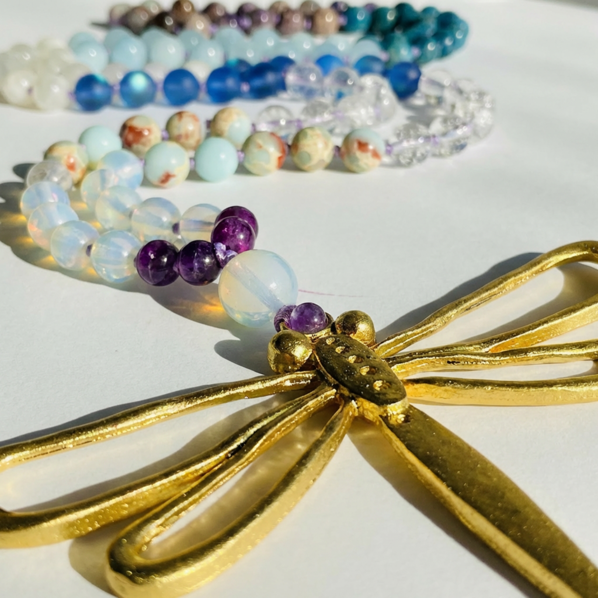 Colorful beaded mala necklace with a gold dragonfly on a white background