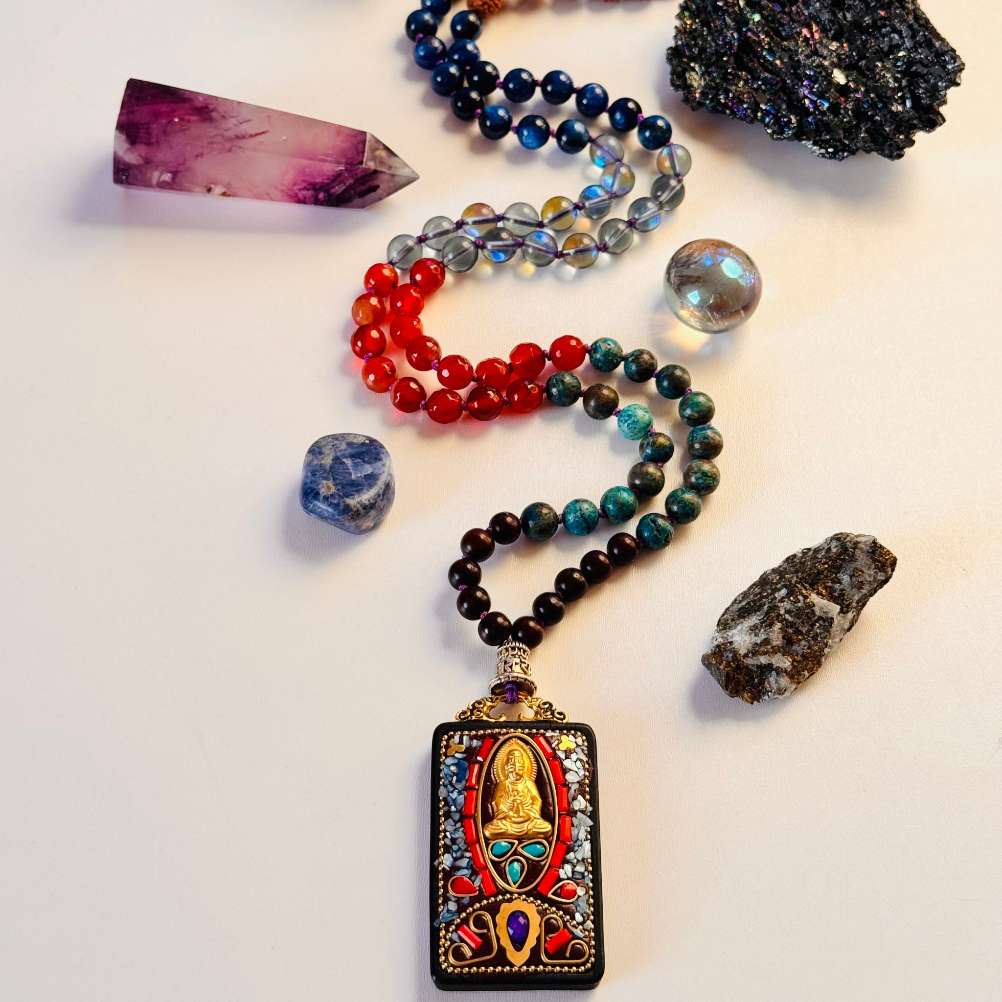 A colorful assortment of hand-beaded gemstone meditation beads featuring various stones and a hand-carved wooden Buddha pendant.