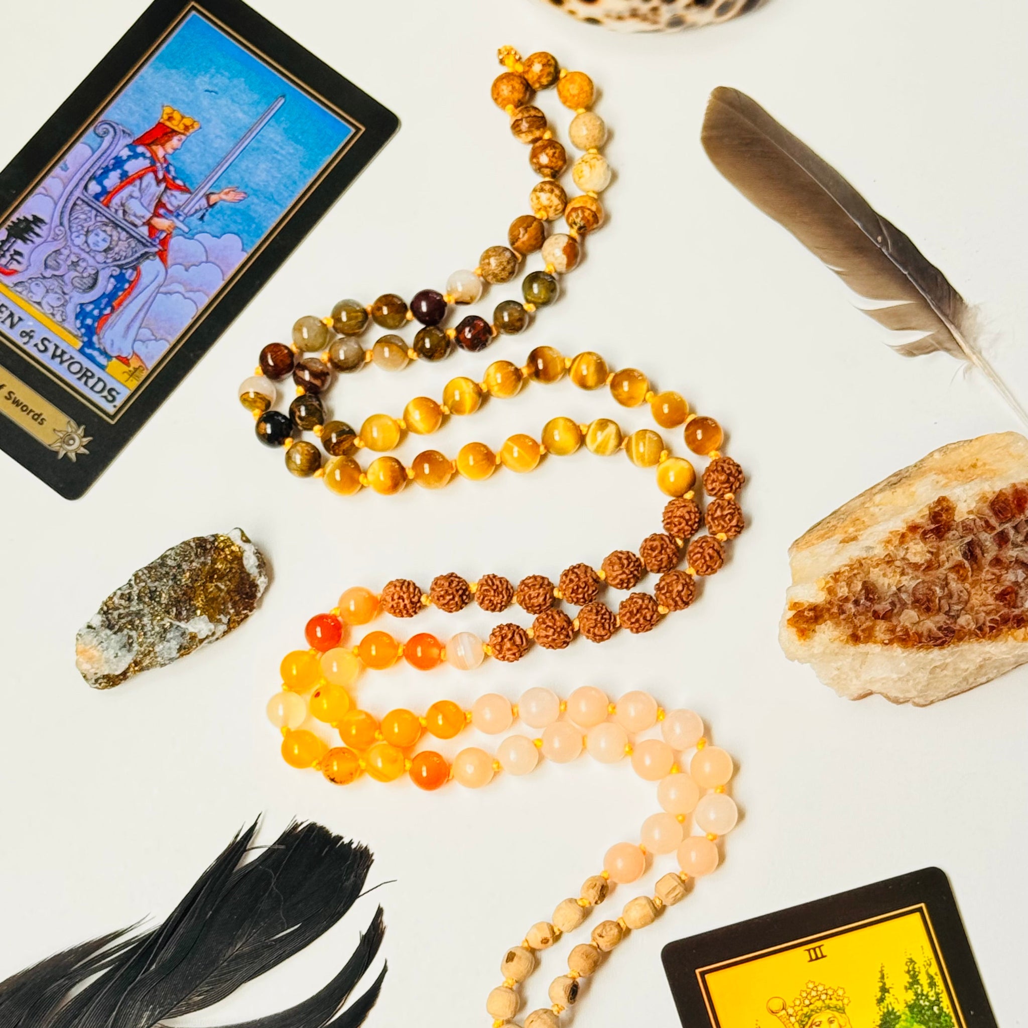 Decorative arrangement of tarot cards, beads, feathers, and crystals on a white surface