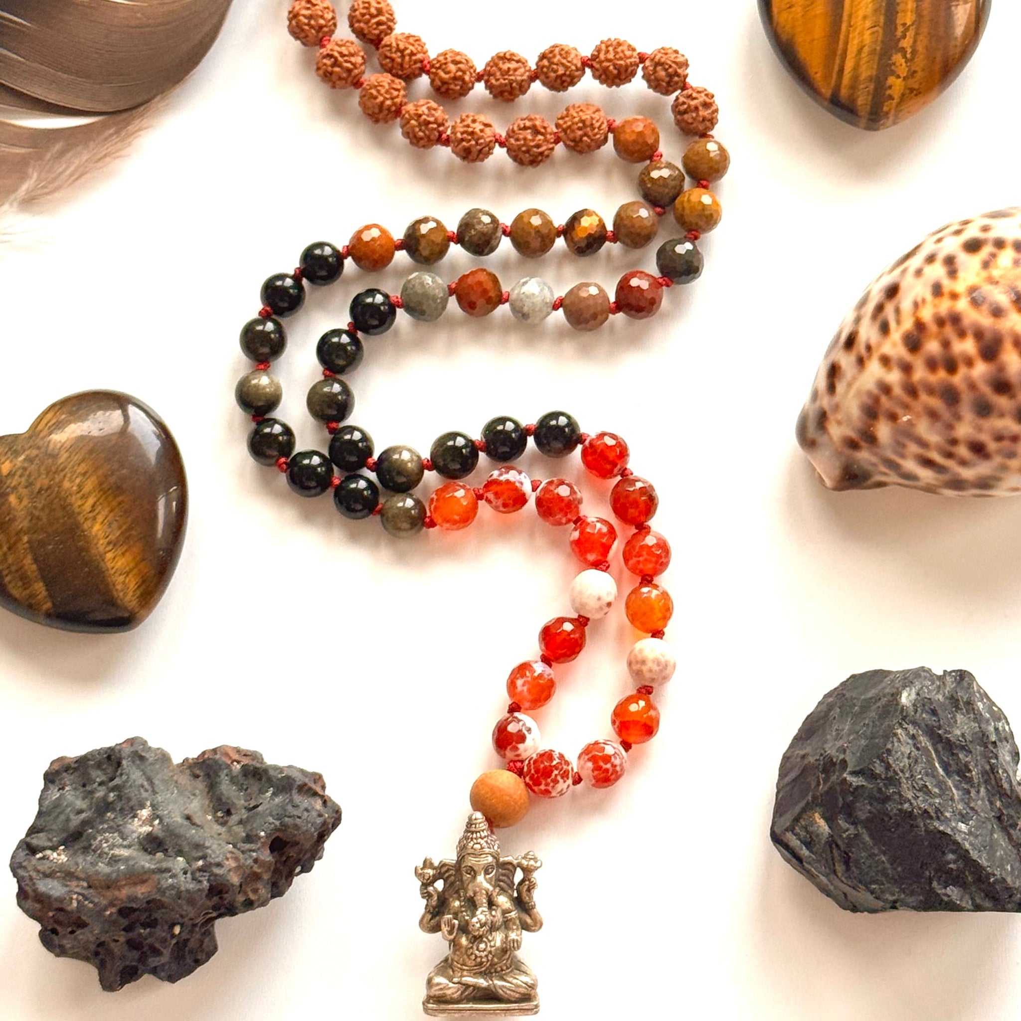 Necklace with beads and a pendant surrounded by stones and shells on a white background