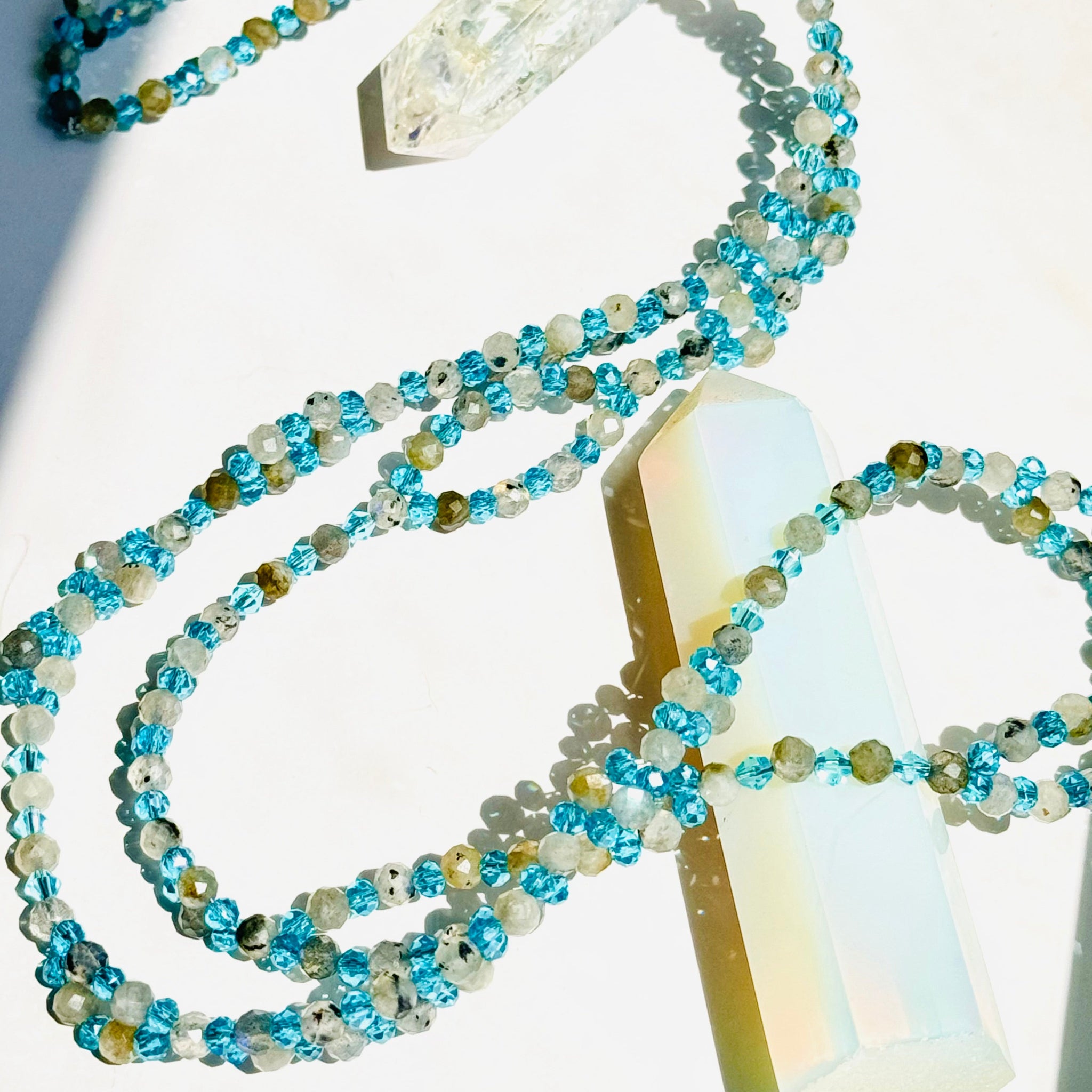 Beaded moonstone Tantric necklace with blue beads on white surface and white crsytal