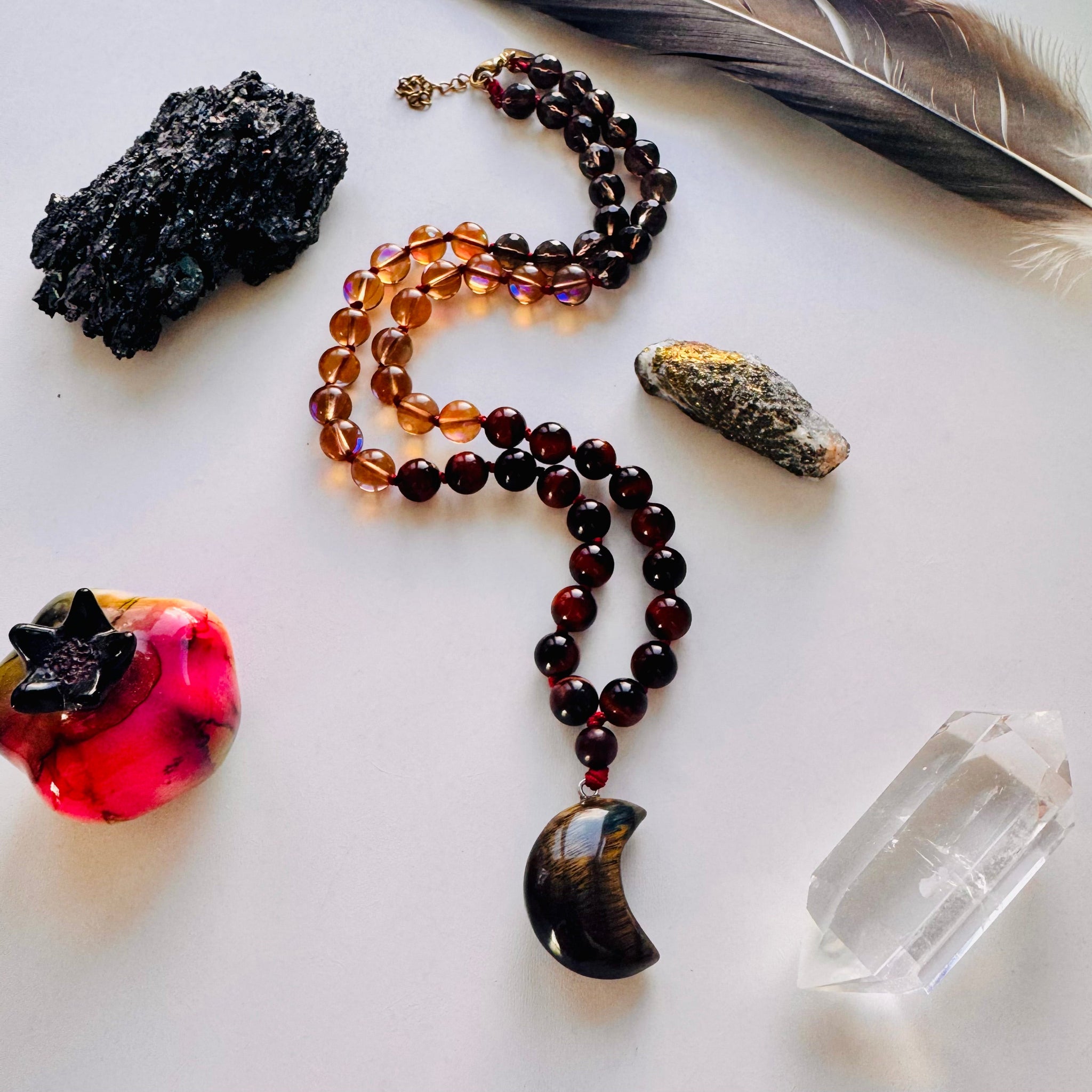 Necklace with beads and a pendant on a white surface with crystals and a feather.