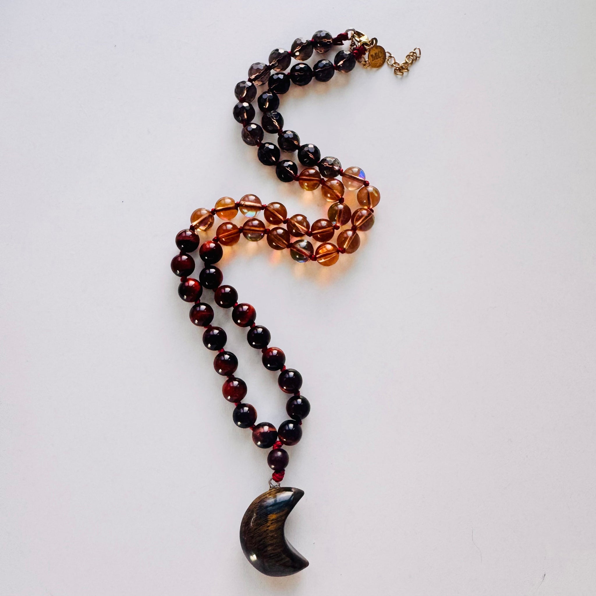 Necklace with beads and a pendant on a white surface with crystals and a feather.