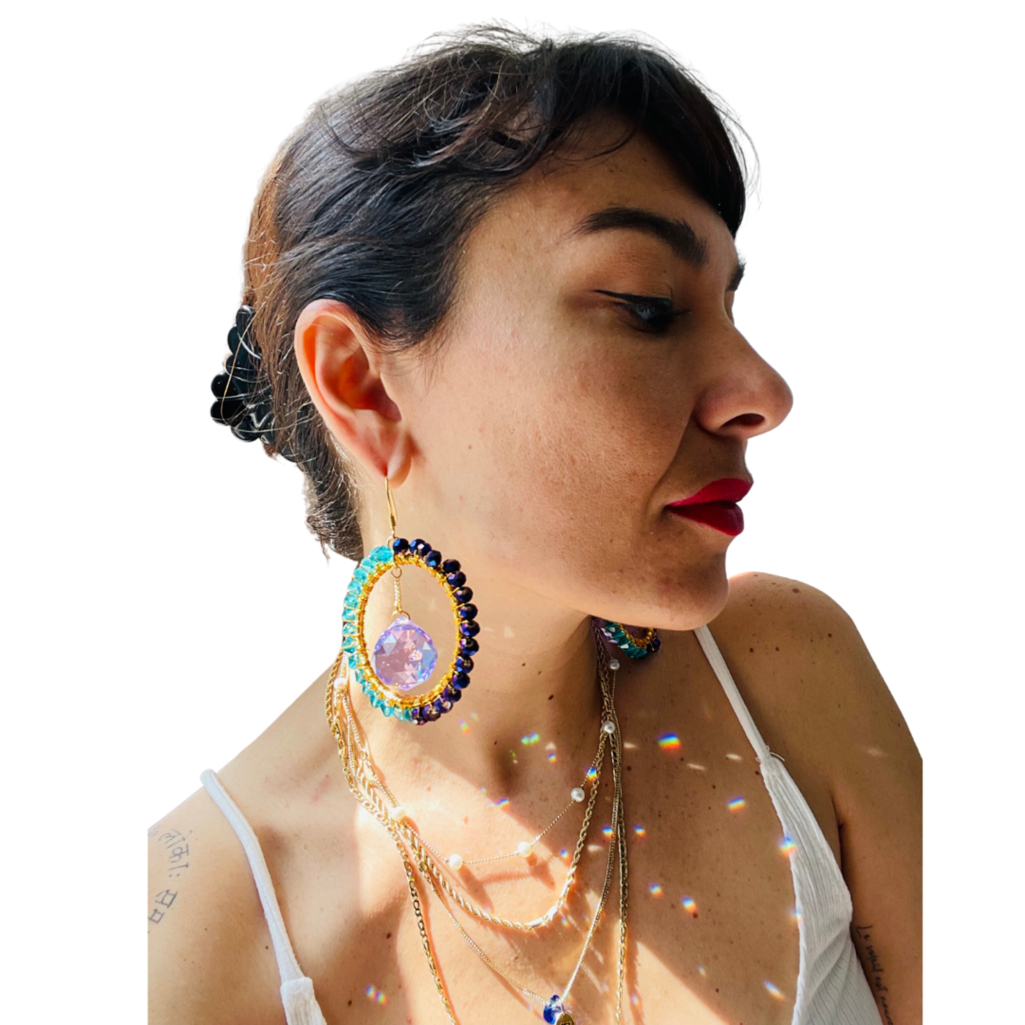 A pair of magnetic suncatcher earrings with blue and green stones set in a gold-tone frame, designed to dangle and reflect light on a model.