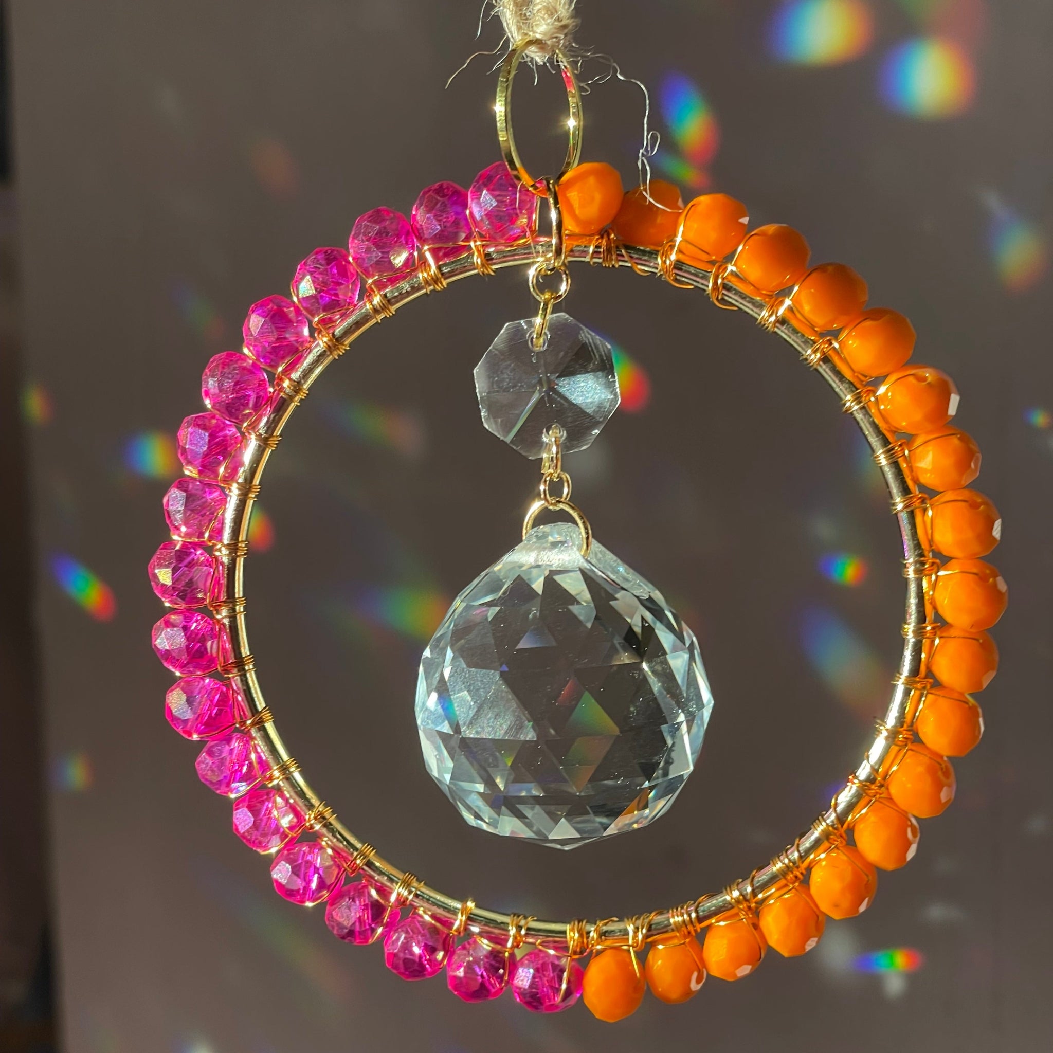 Magenta and orange wire wrapped crystals over brass circle with prism in the middle creating rainbows on the wall