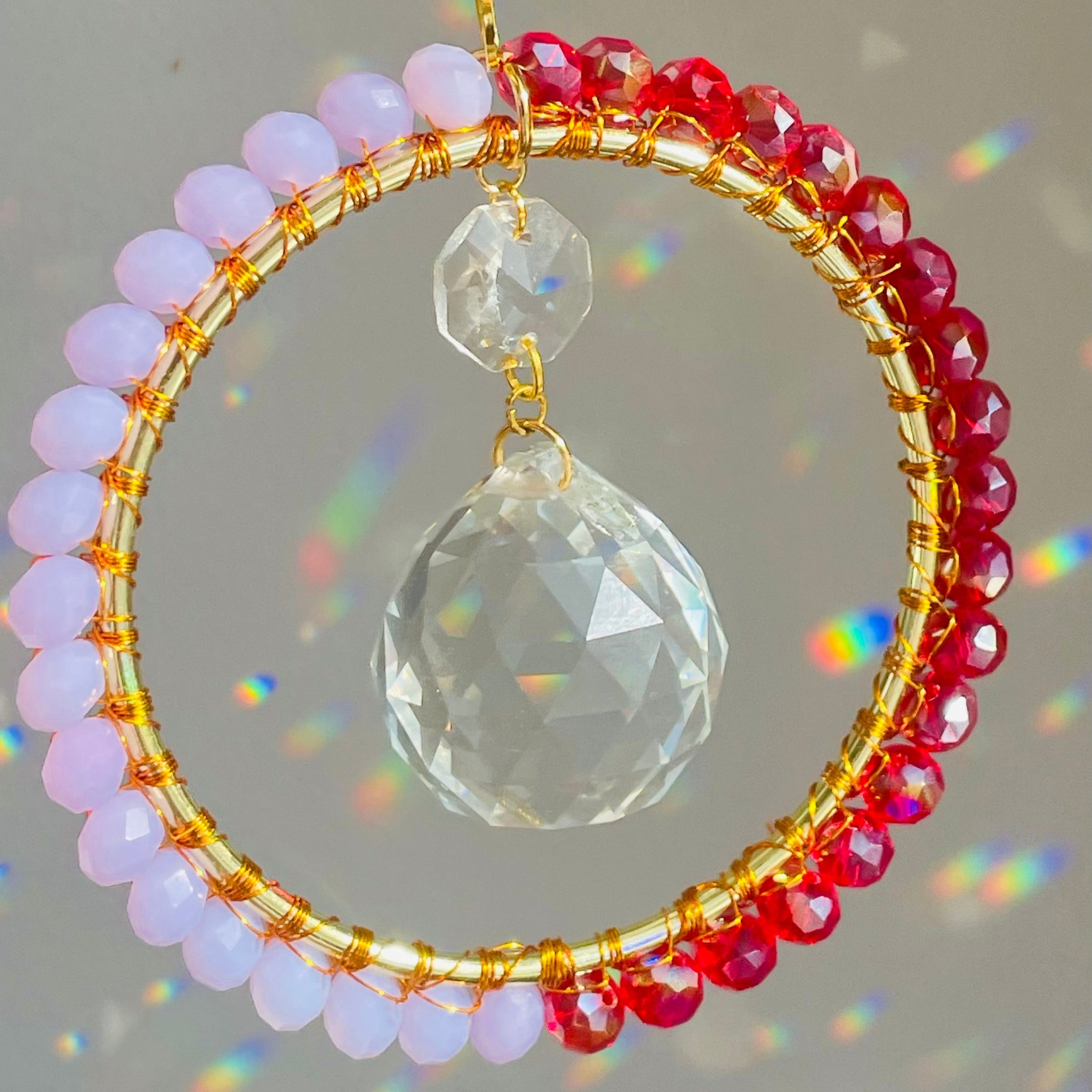 red and lavender crystals wire wrapped on brass with prism in the middle creating rainbows in front of white wall