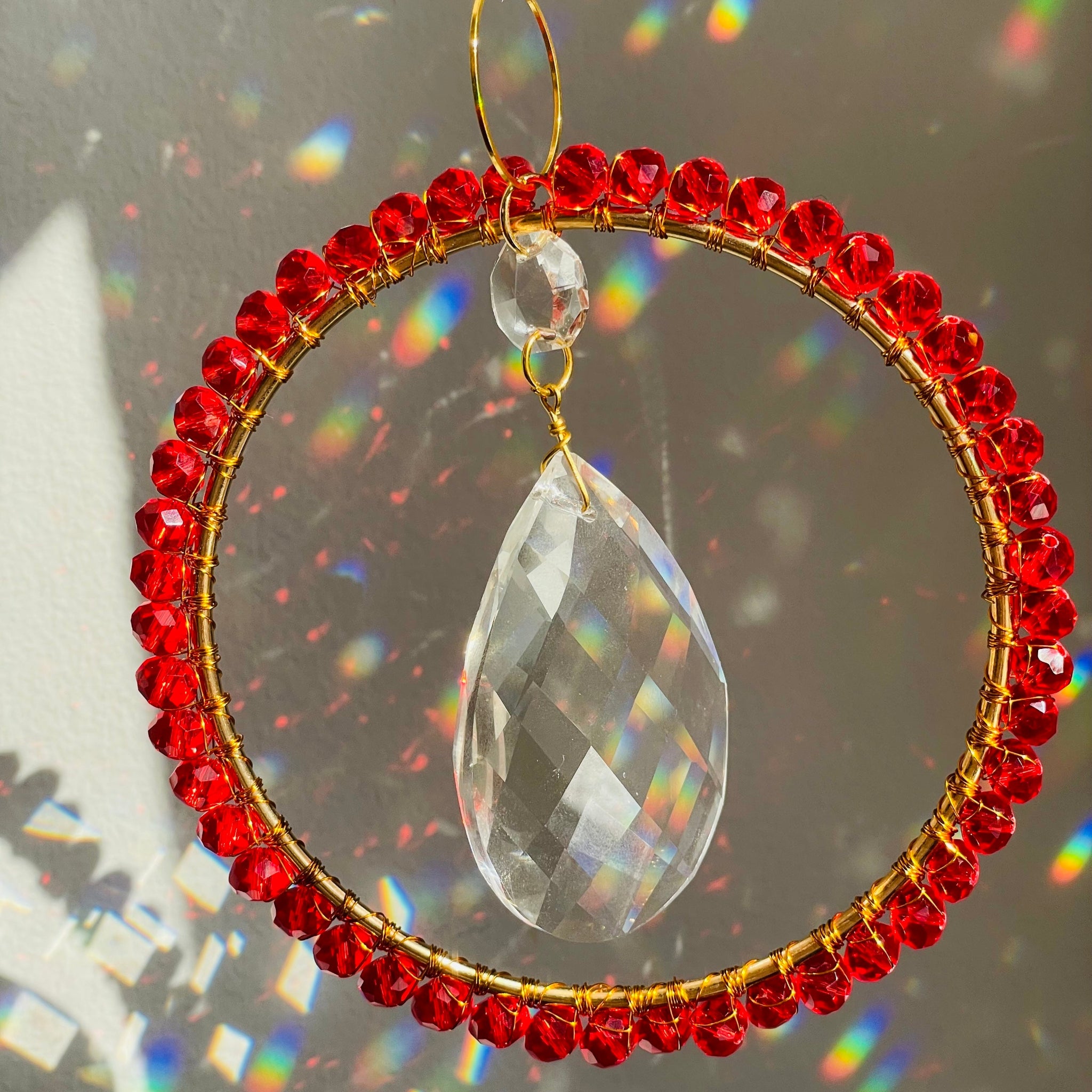 Decorative hanging ornament with red beads and a clear teardrop crystal on a dark background.