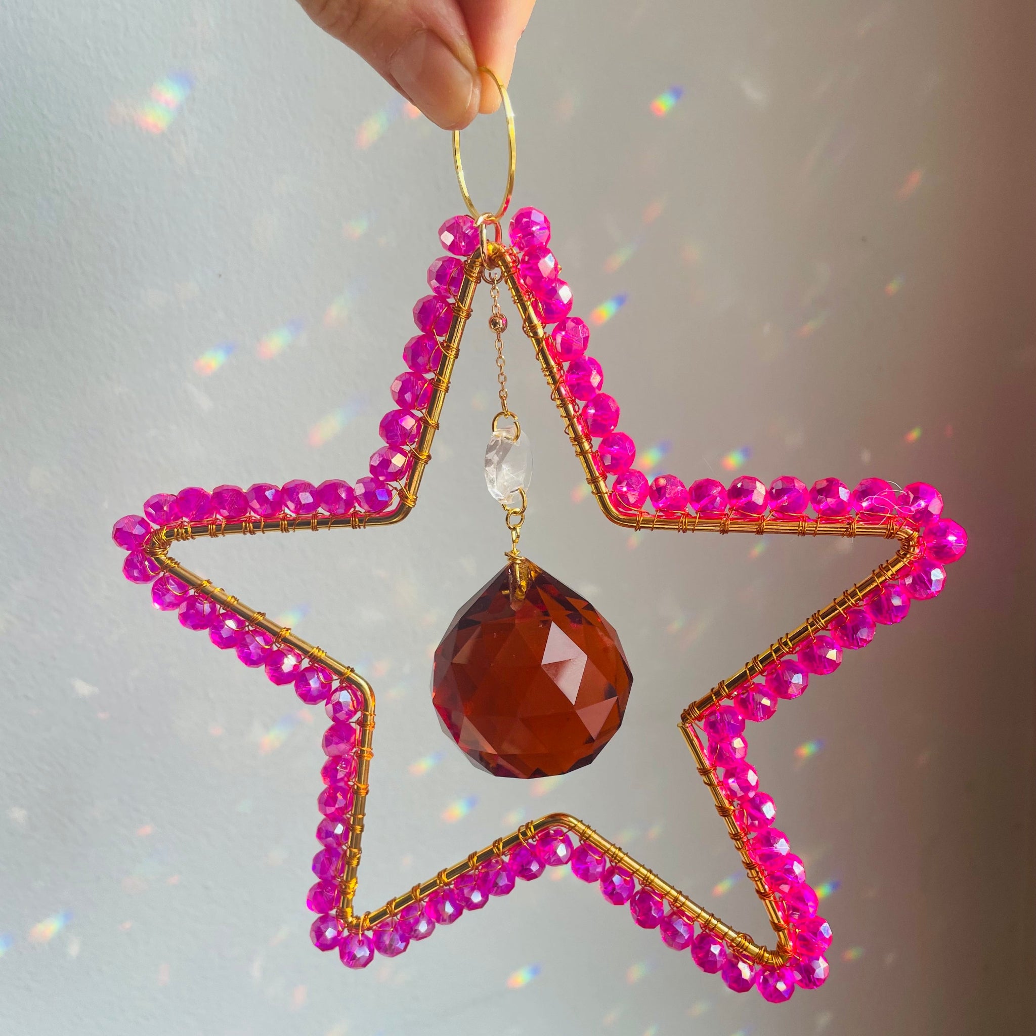 Star-shaped ornament with pink beads and a brown teardrop pendant on a soft gray background