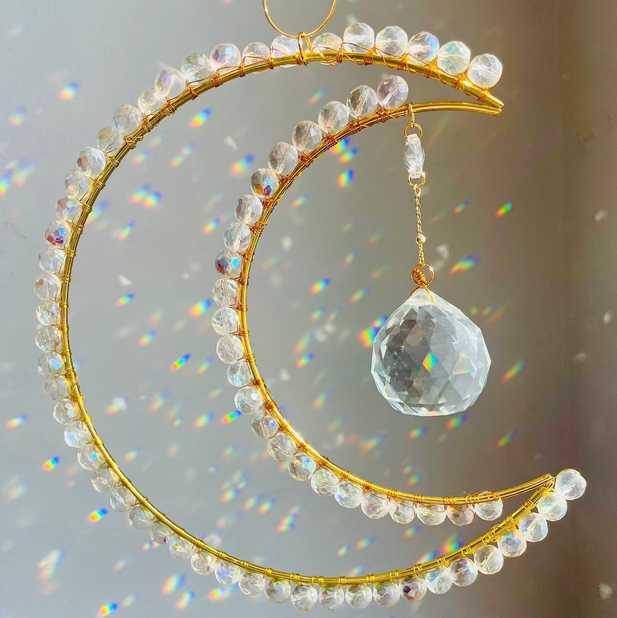 gold crescent wrapped with clear crystals with a big prism hanging in the middle creating rainbows