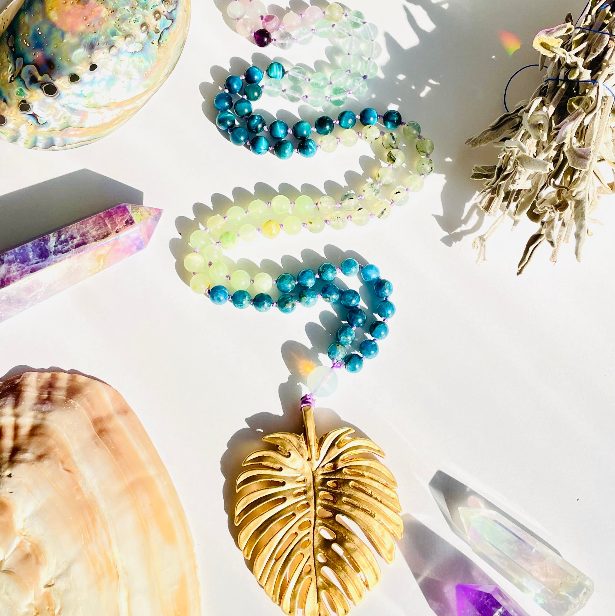 Collection of jewelry and decorative items including a beaded bracelet, crystal, and leaf-shaped object on a white surface.
