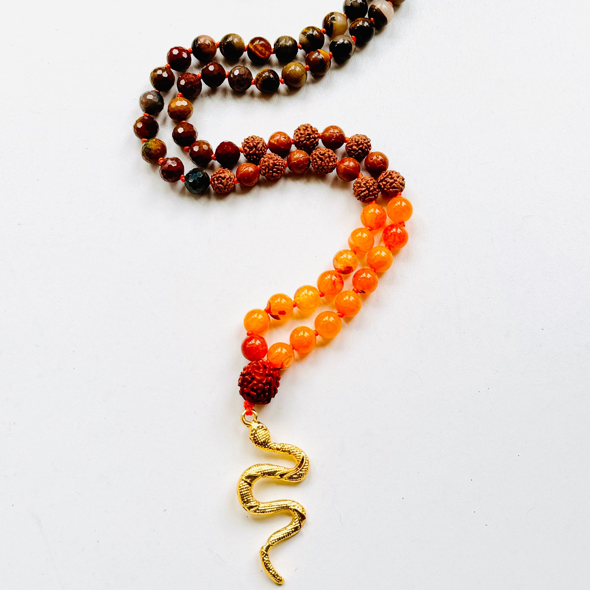 A collection of beaded necklaces with a brass serpent pendant on white surface.
