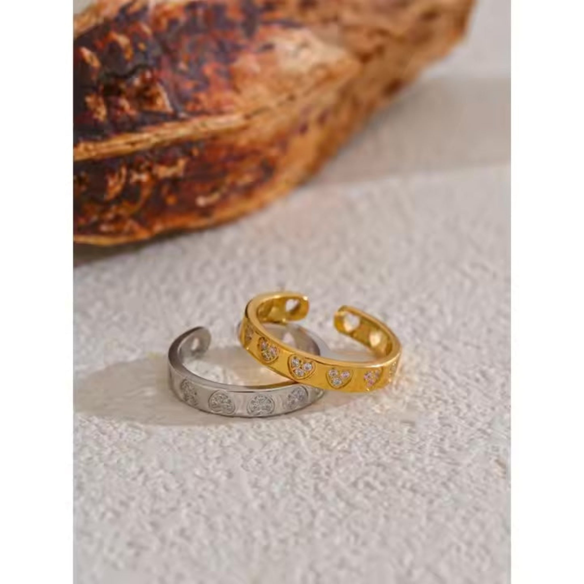 Two open rings with heart patterns on a textured surface.