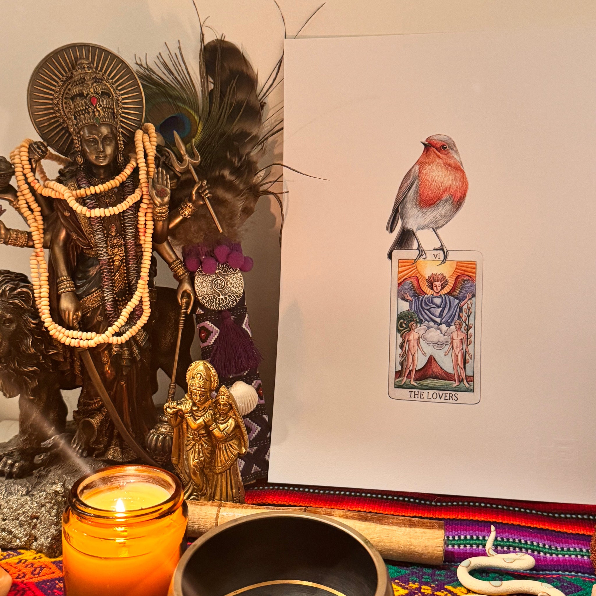 eclectic collection of objects including a tarot card, feathers, a candle, and a colorful fabric on a neutral background