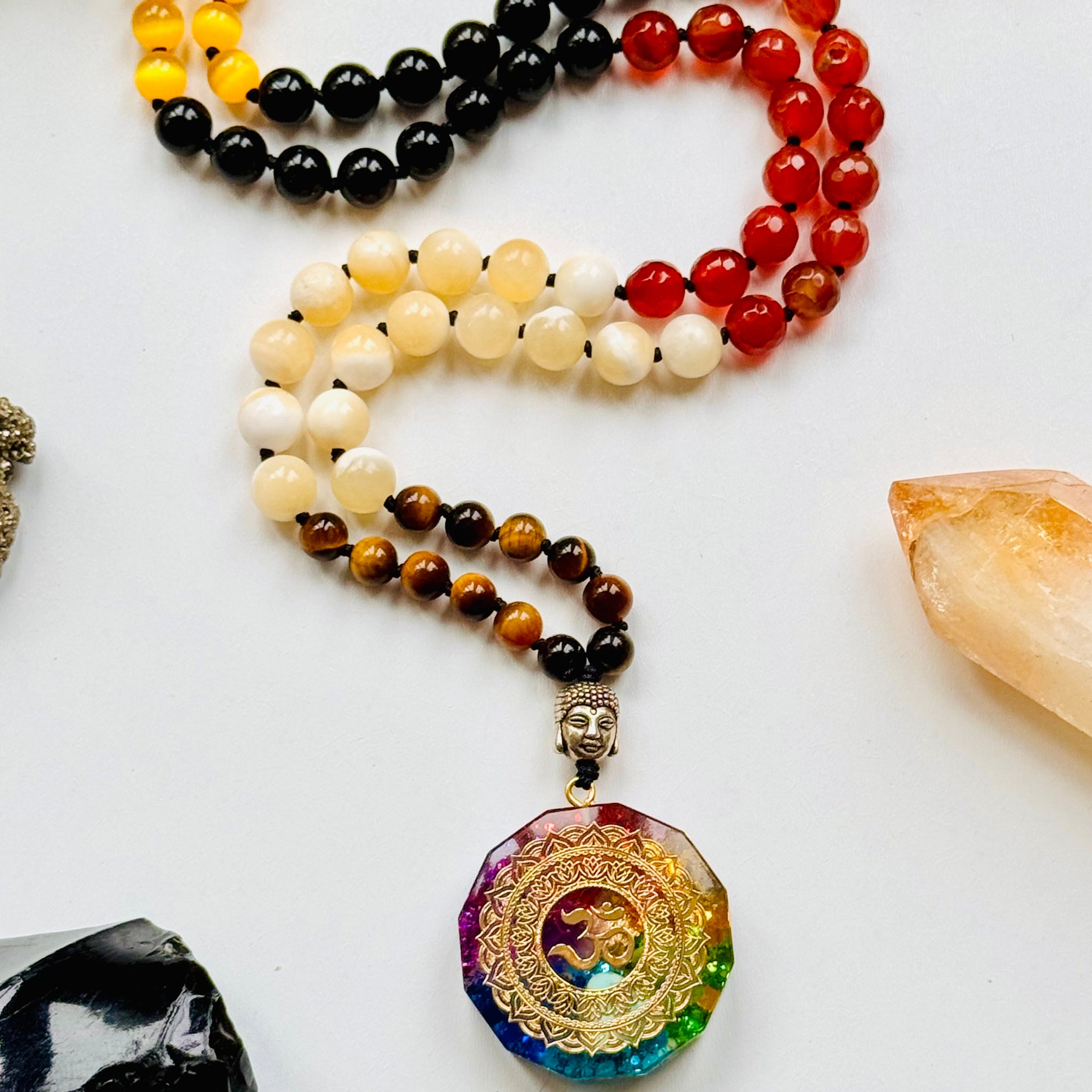 A variety of colorful gemstone beads with Om organite pendant and crystals on white surface.