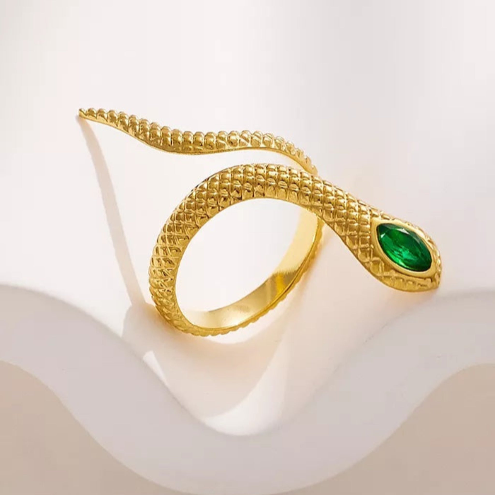 Gold snake-shaped ring with a green gem on a white background