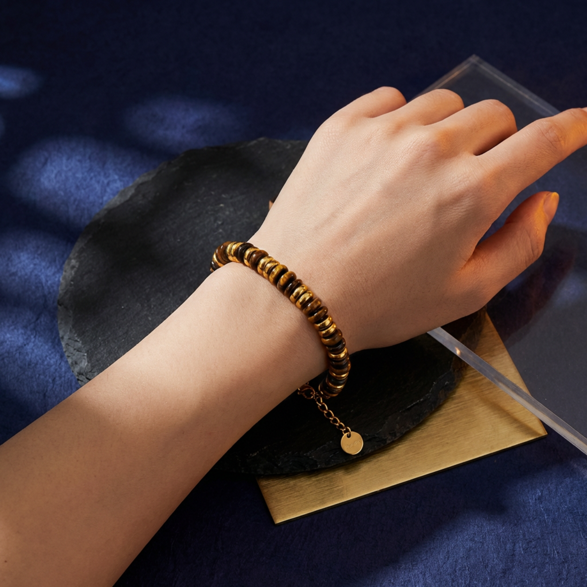Hand wearing a gold bracelet on a dark surface with a blue background
