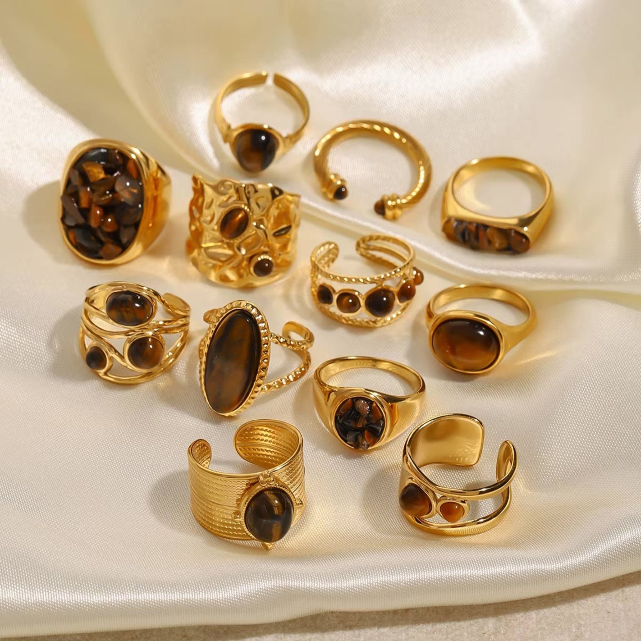 Collection of gold rings with brown gemstones on a white fabric background