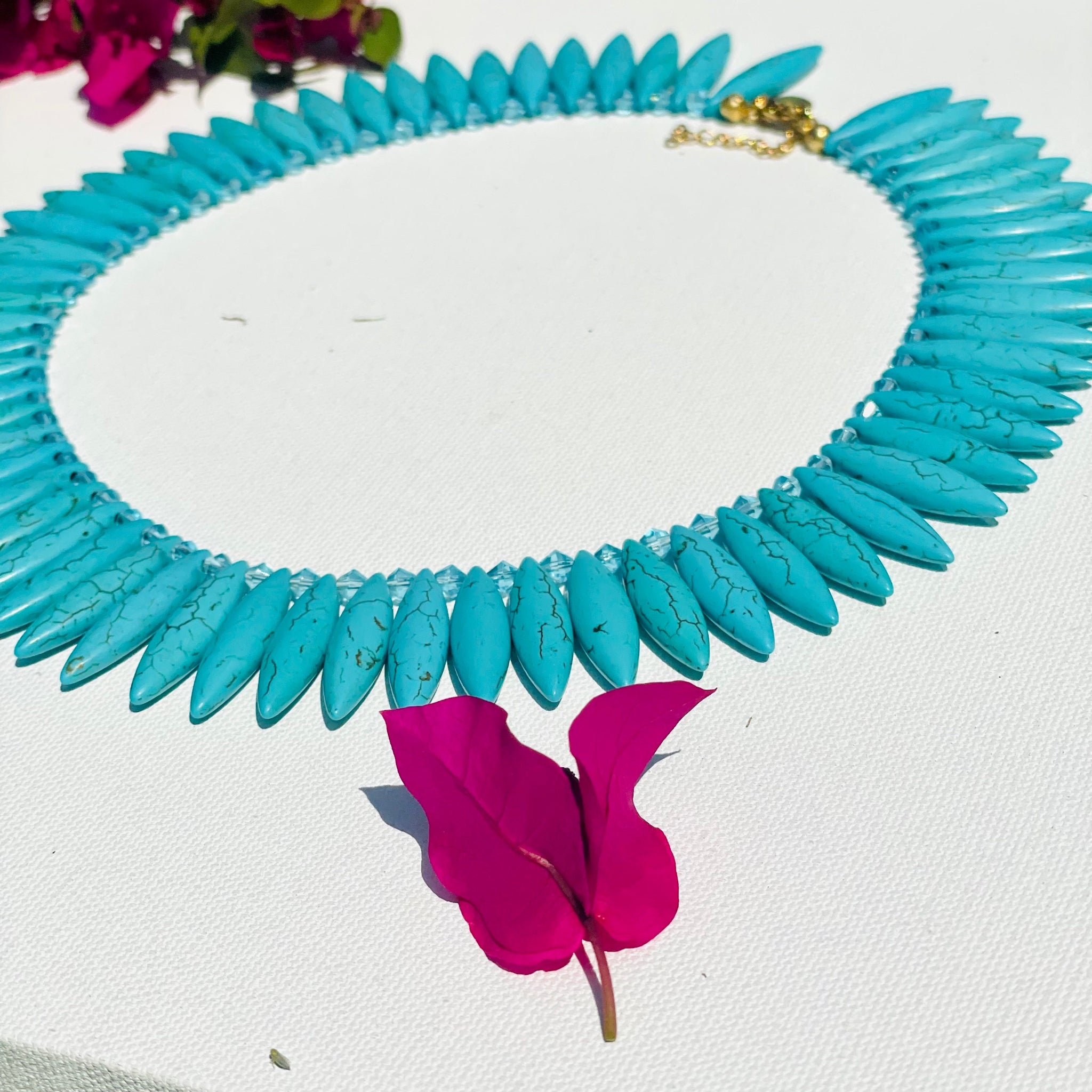 Spike cut turquoise necklace with pink flowers on a white surface