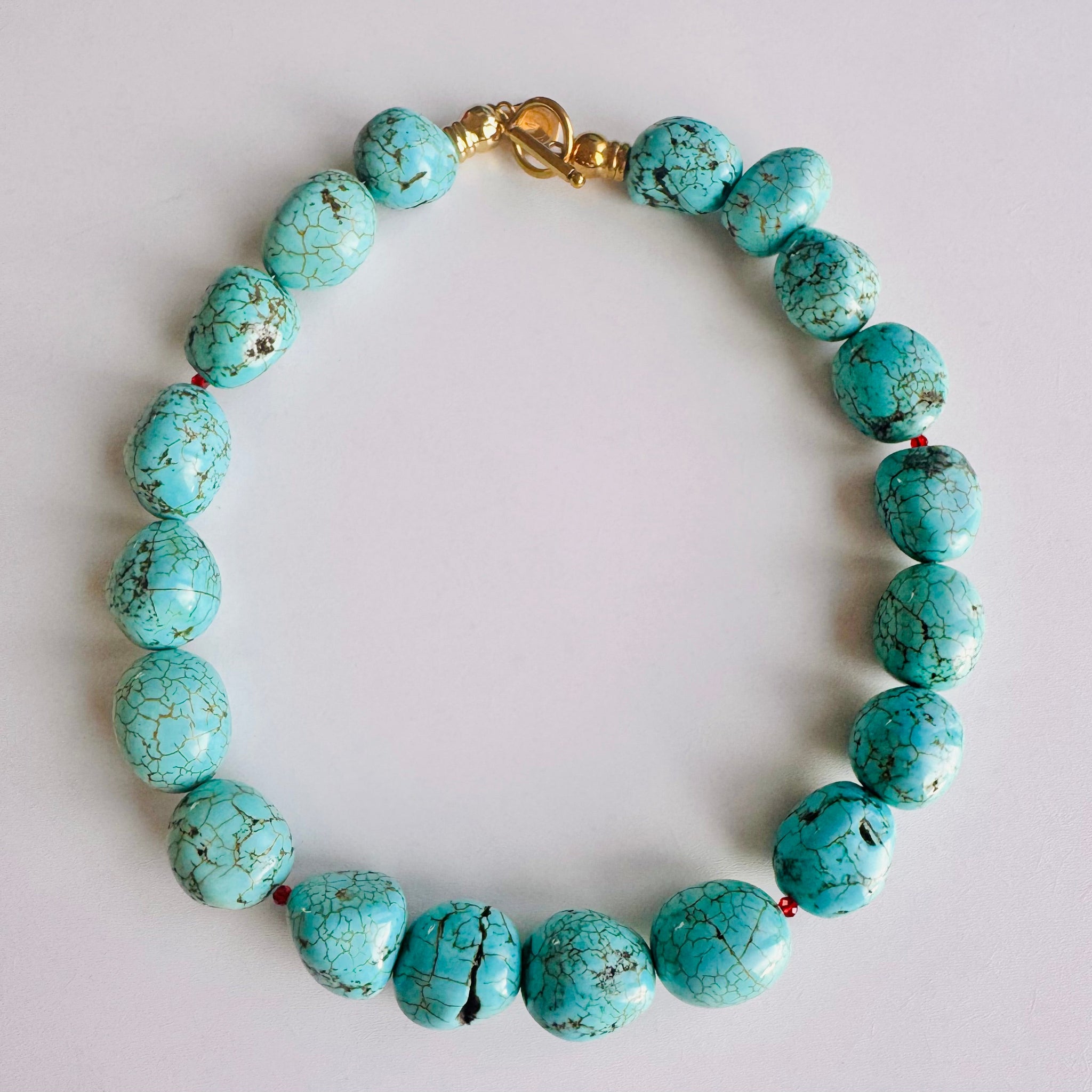 Turquoise beaded necklace with a gold clasp on a light gray background
