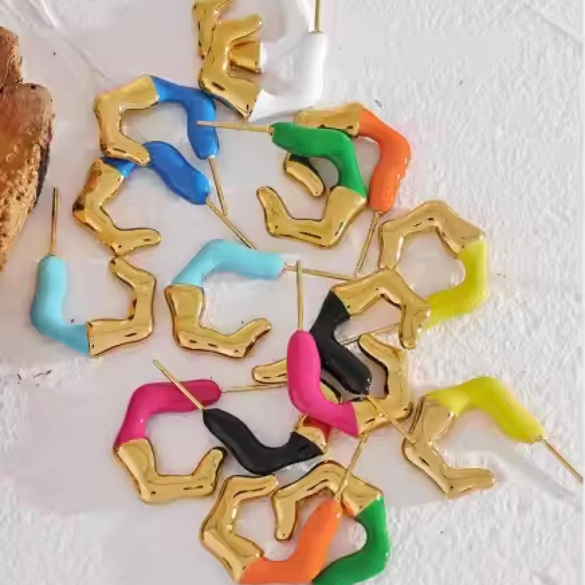 A collection of colorful enamel stud earrings in gold-plated sterling silver, displayed in a radiating pattern on a light background.