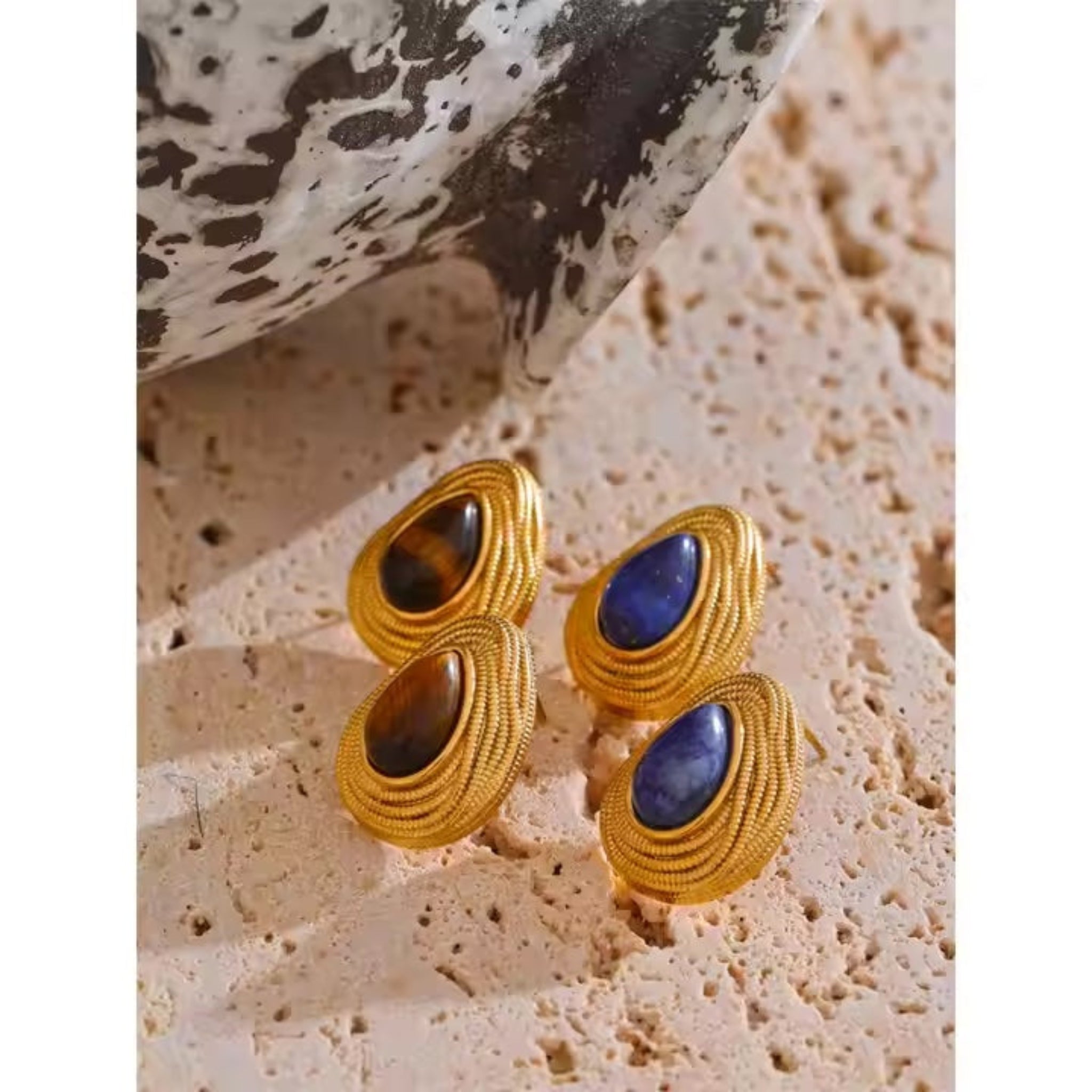 Pair of gold earrings with gemstones on a textured stone surface.