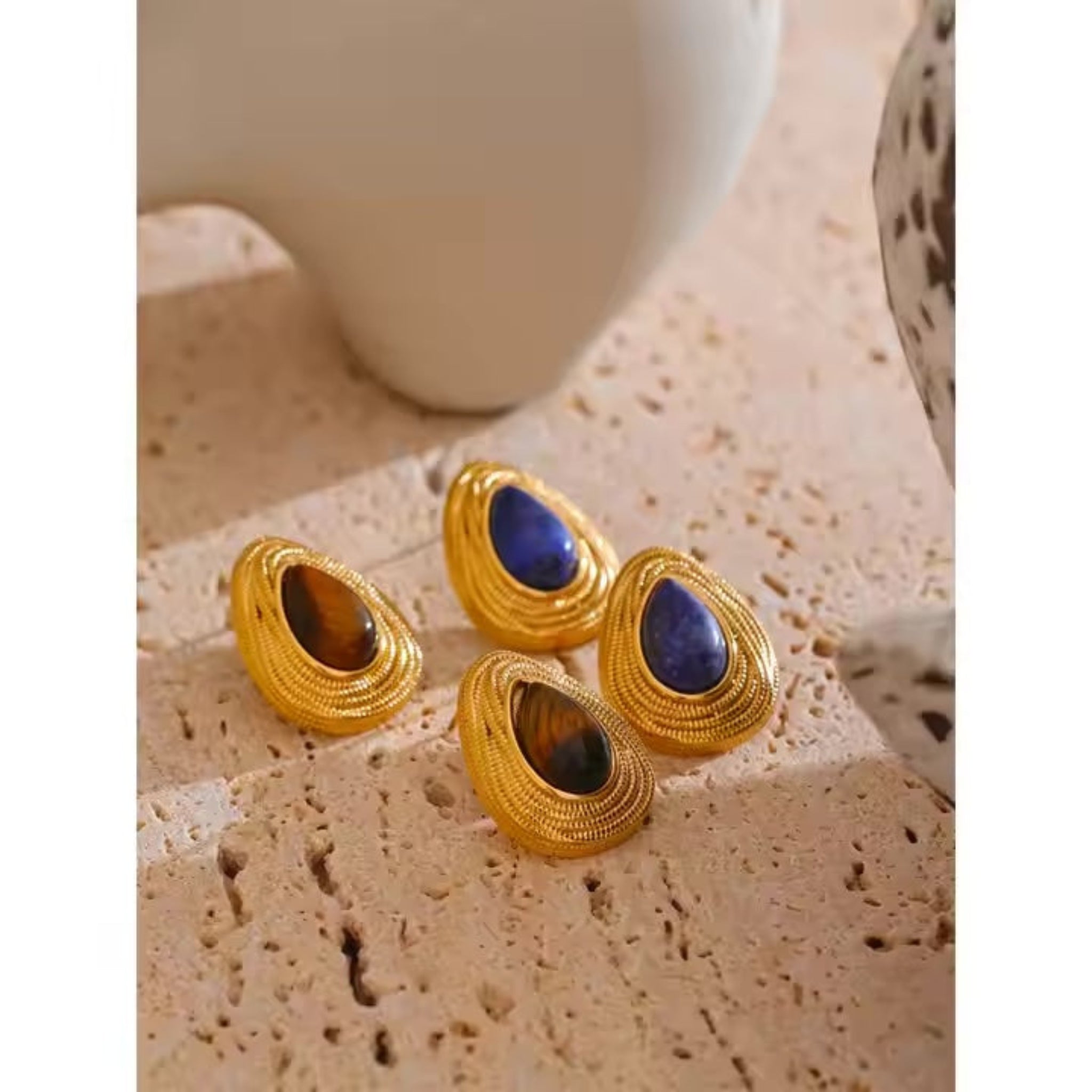 Gold earrings with gemstones on a textured surface.