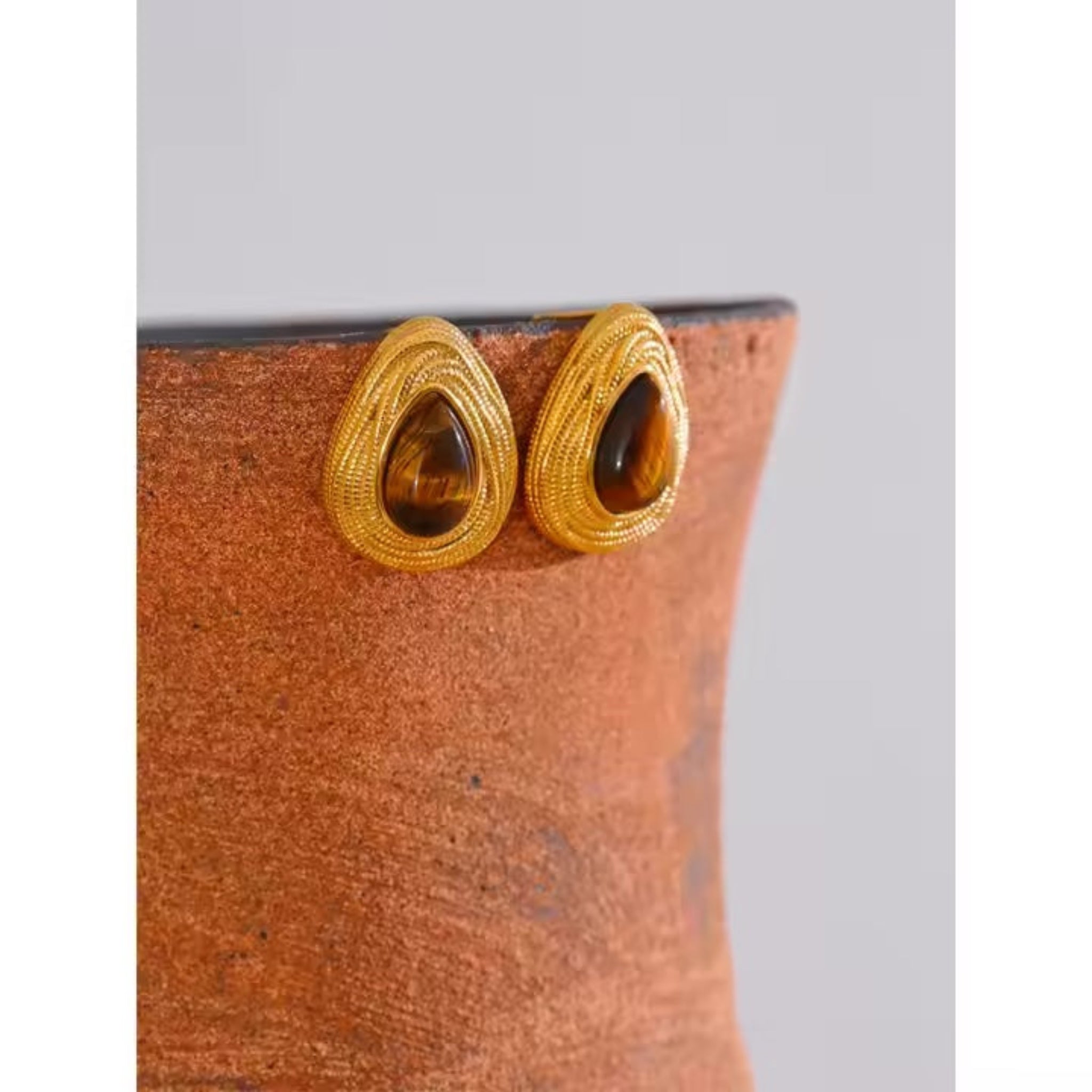 Pair of gold earrings on a textured brown surface.