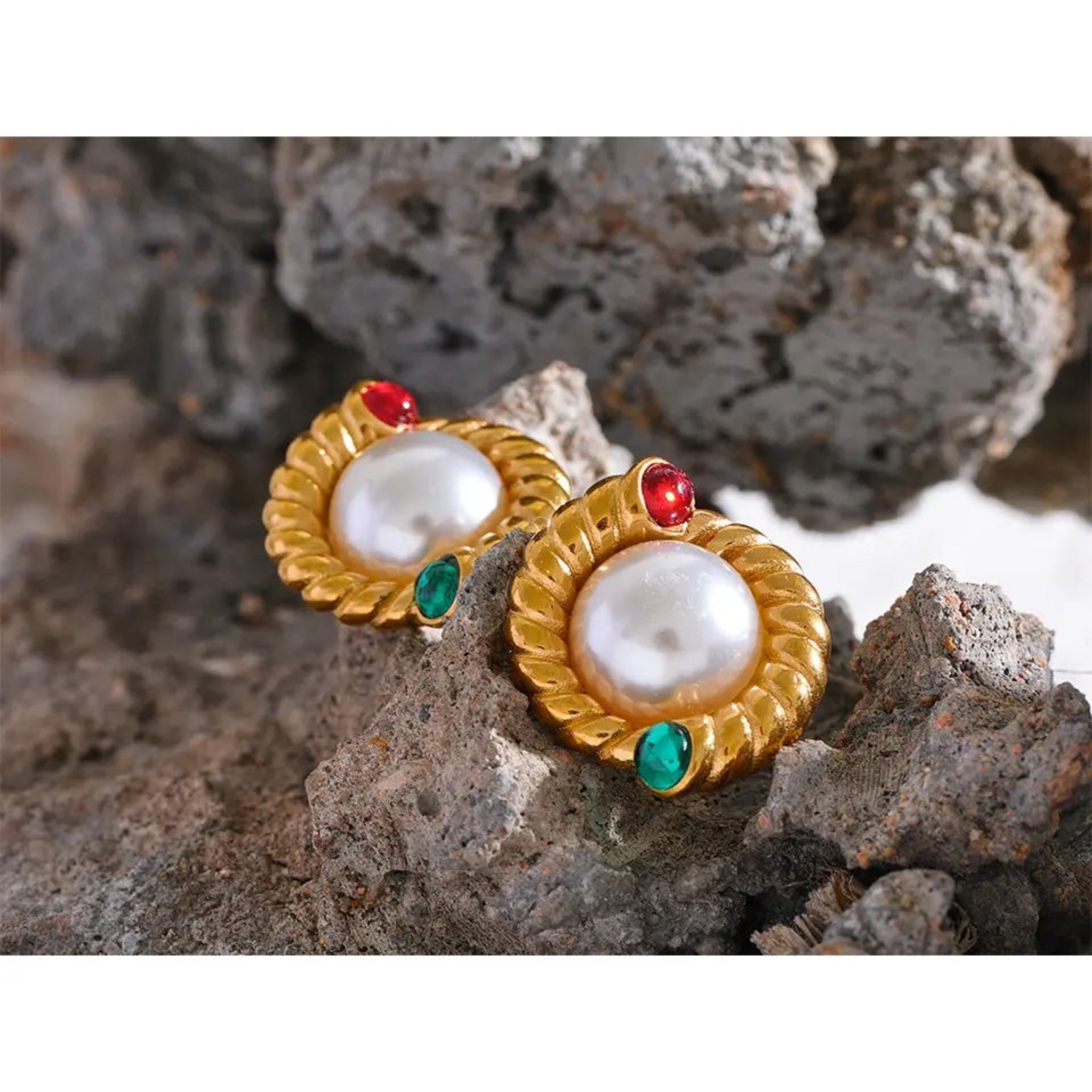 A pair of vintage pearl stud earrings with gold accents and red and green details on a textured background.