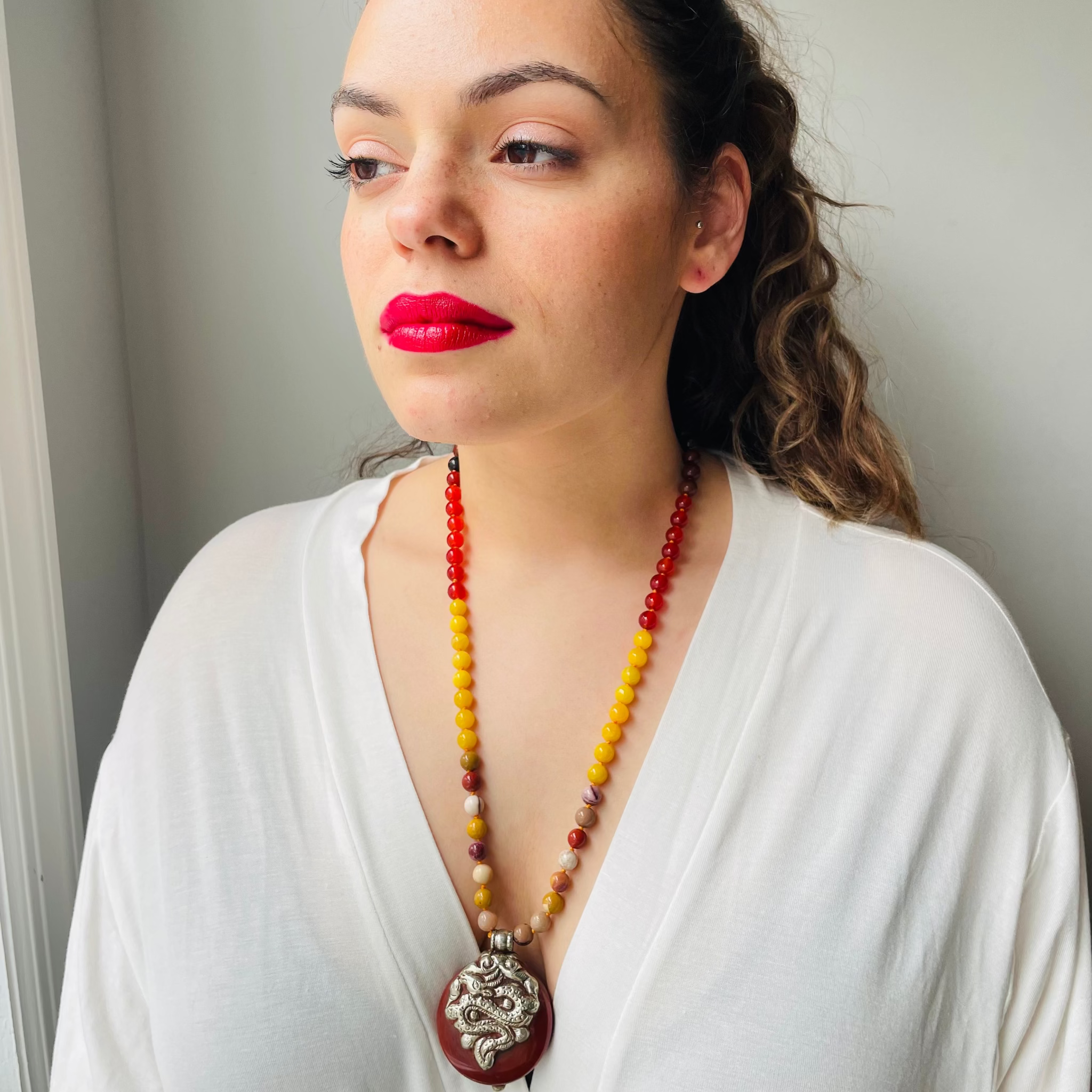Woman wearing a colorful beaded necklace with a pendant against a neutral background