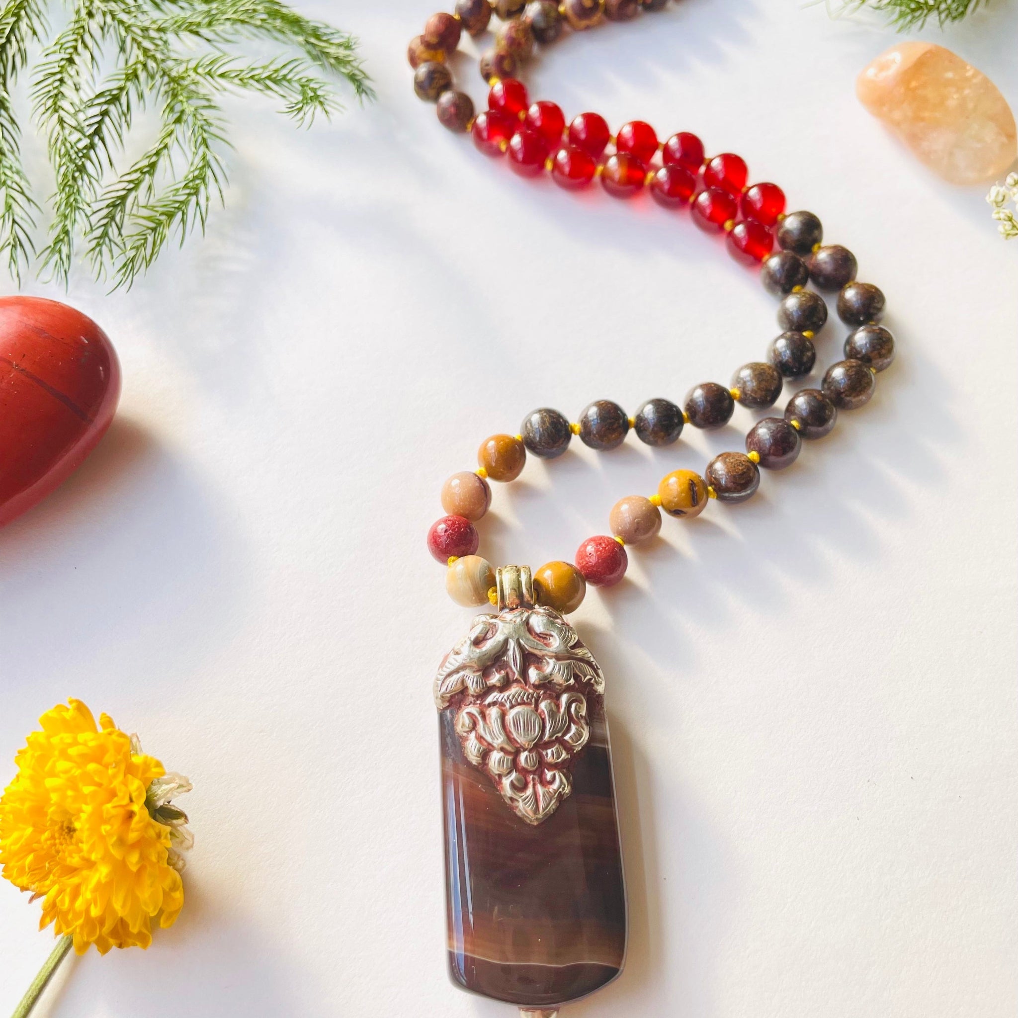 Necklace with a large pendant on a white surface with greenery and stones.