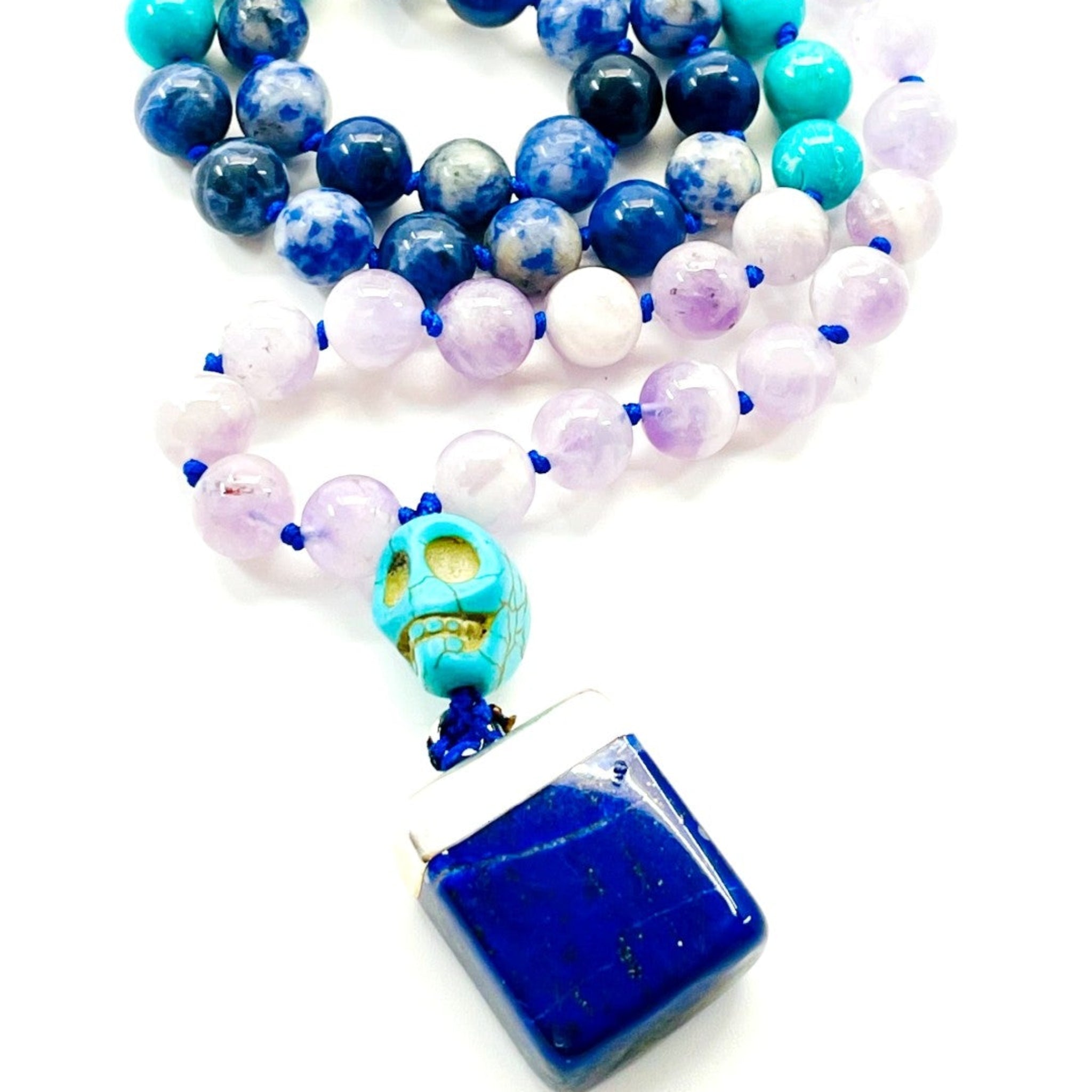 A colorful half mala necklace with sodalite, turquoise, and amethyst beads, and a lapis lazuli pendant in the shape of a skull.