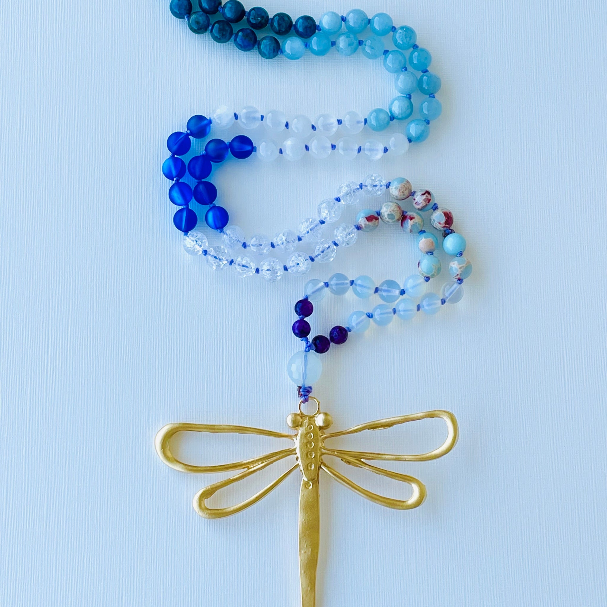 Beaded necklace with a gold dragonfly pendant on a light blue background