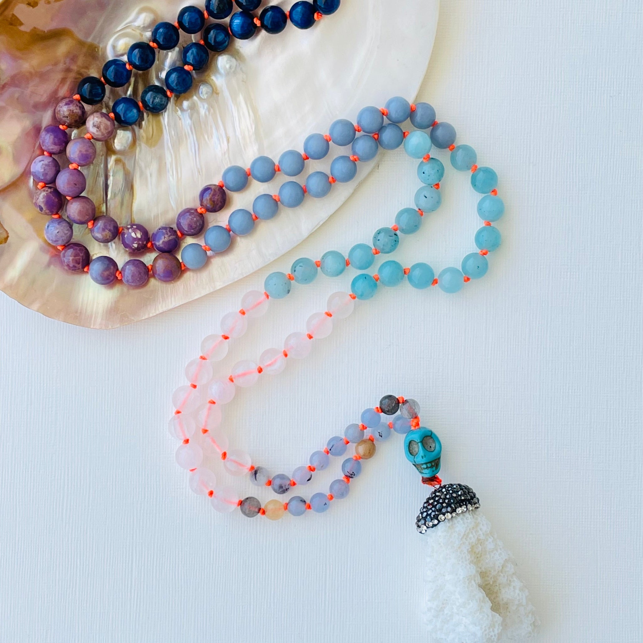 A multicolored beaded mala with purple, blue and lear gemstones with coral pendant.