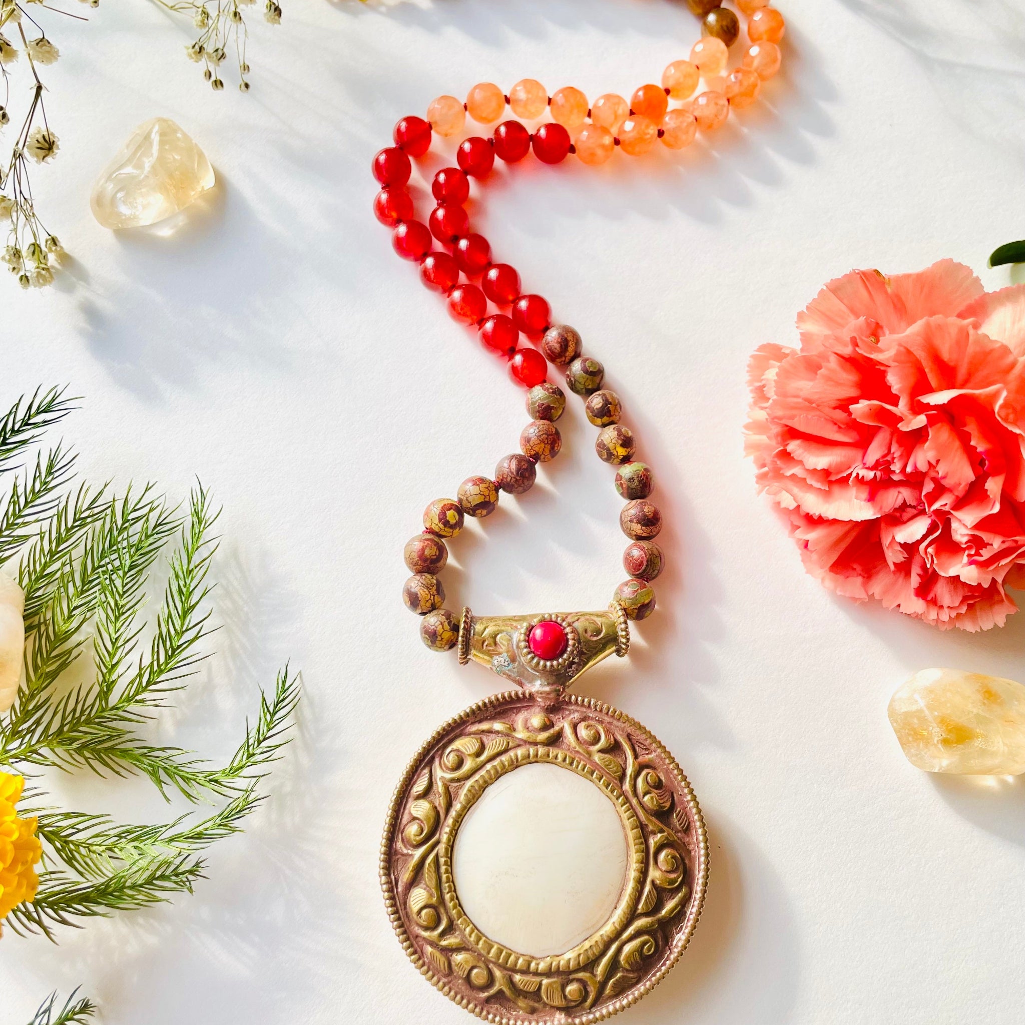 A close-up image of a Focused & Motivated Necklace with a vintage brass pendant, featuring a series of round beads with varying hues and a chain.