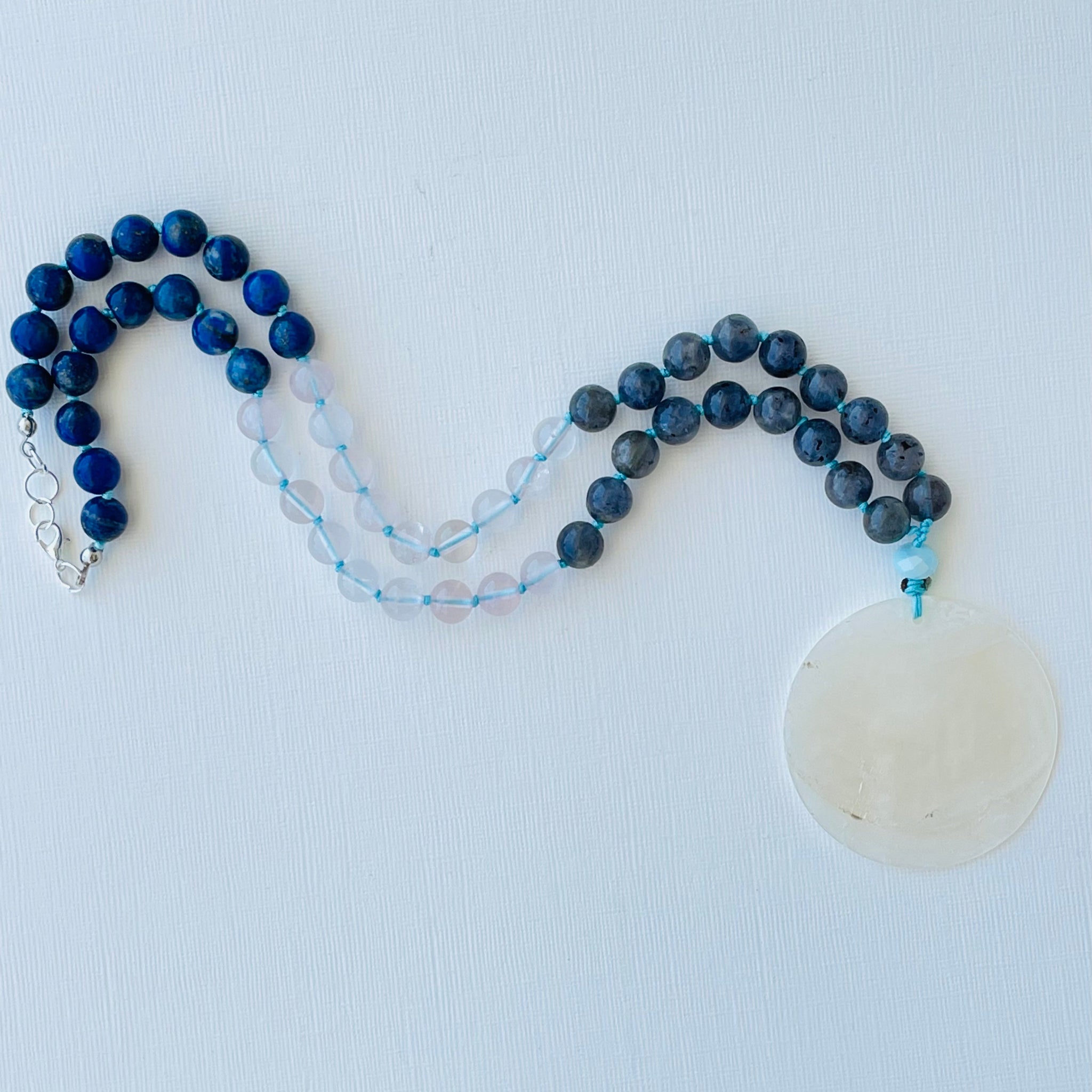 Necklace with blue beads and a white pendant on a light gray background