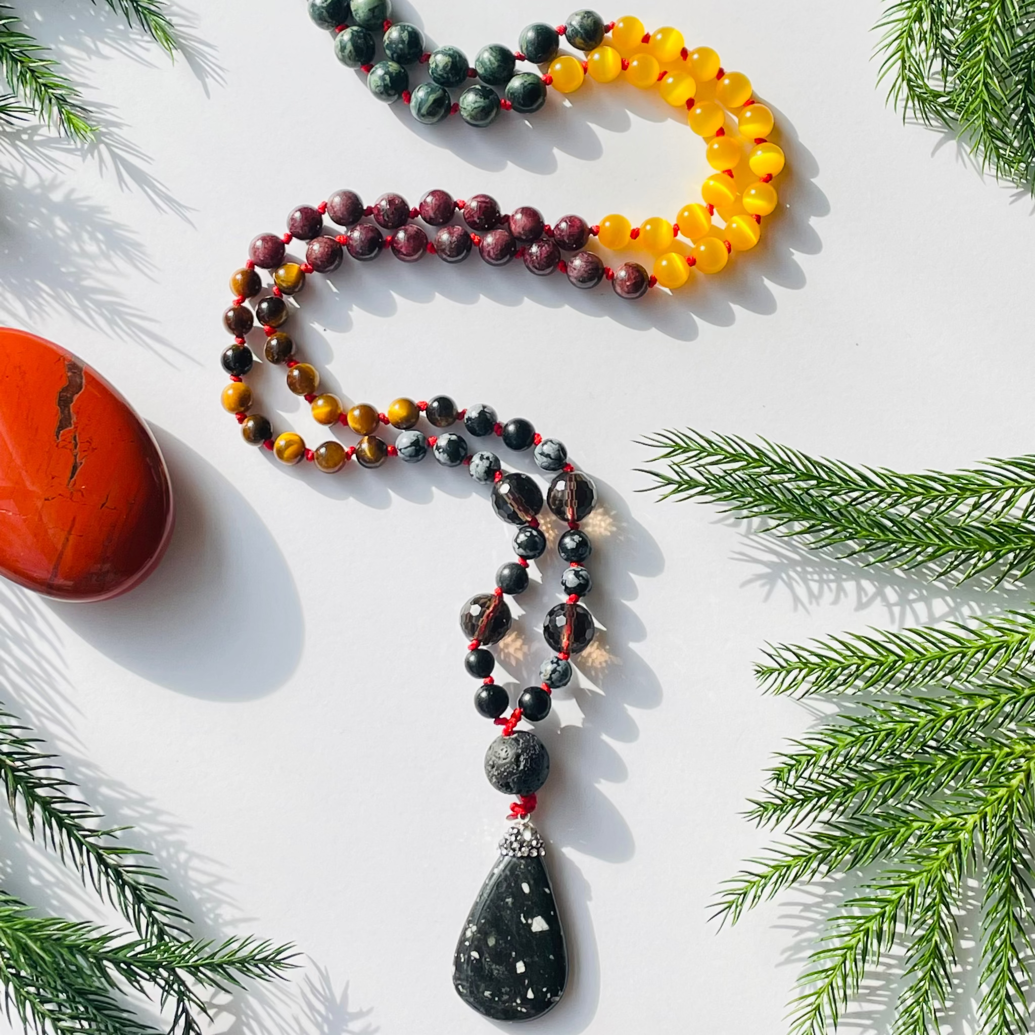 Beaded gemsone necklace on white surface with decorative pine needles