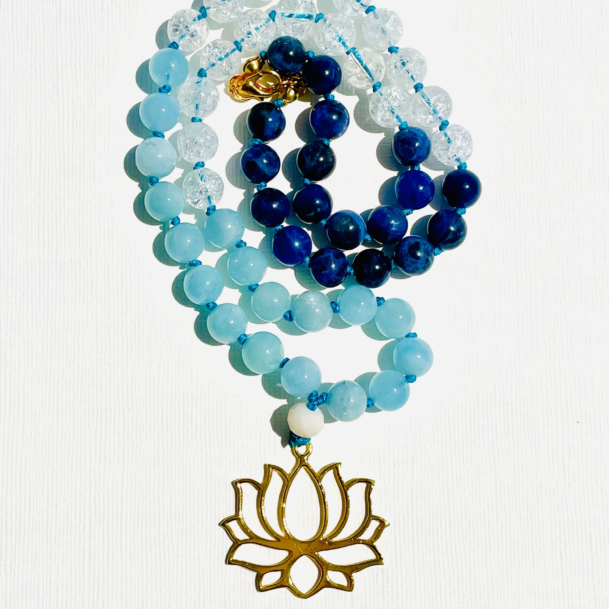 A beaded necklace featuring a lotus flower pendant, predominantly blue and clear quartz beads, and a gold-colored locket.