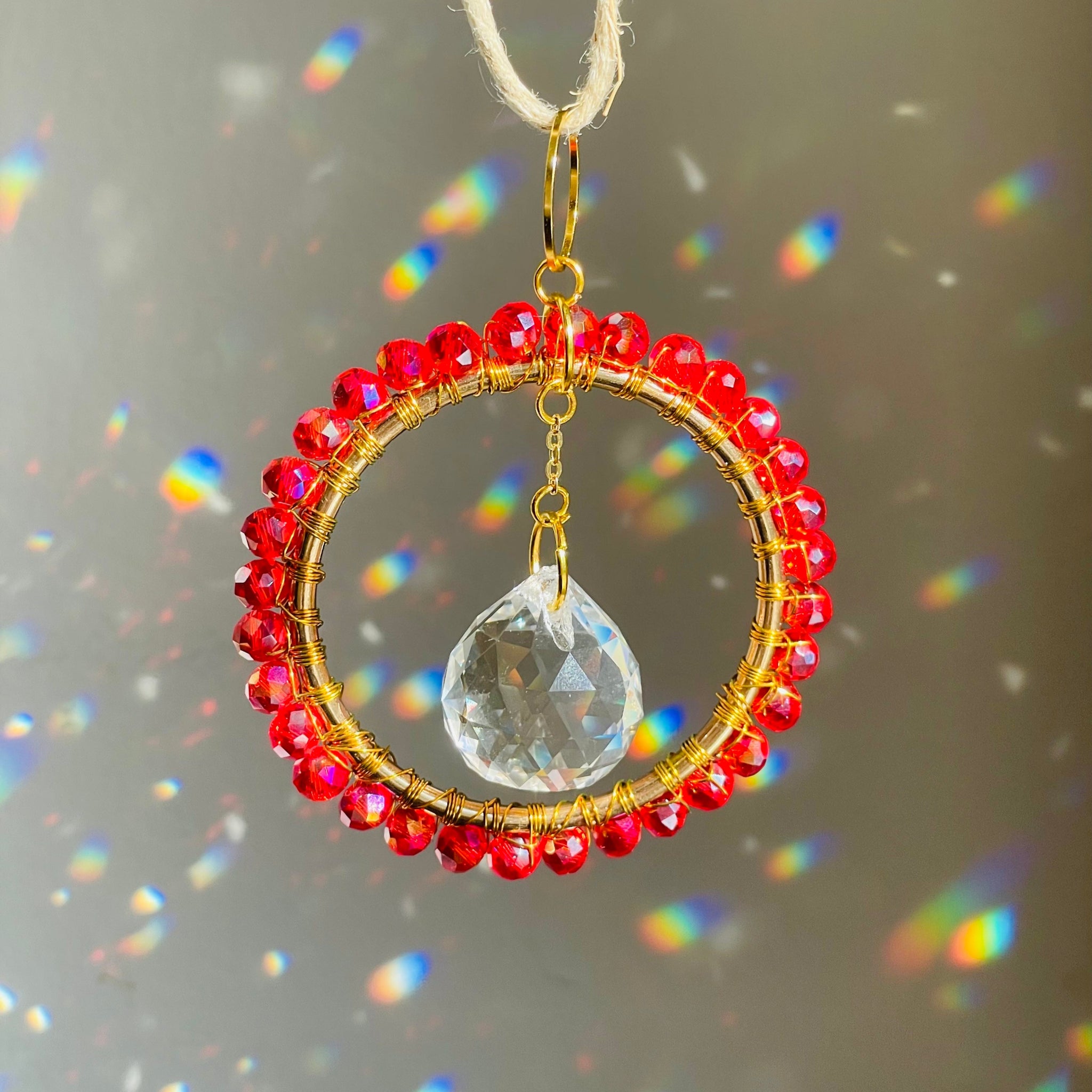 A mini circle suncatcher with a golden frame and clear crystal pendants hung from a chain.